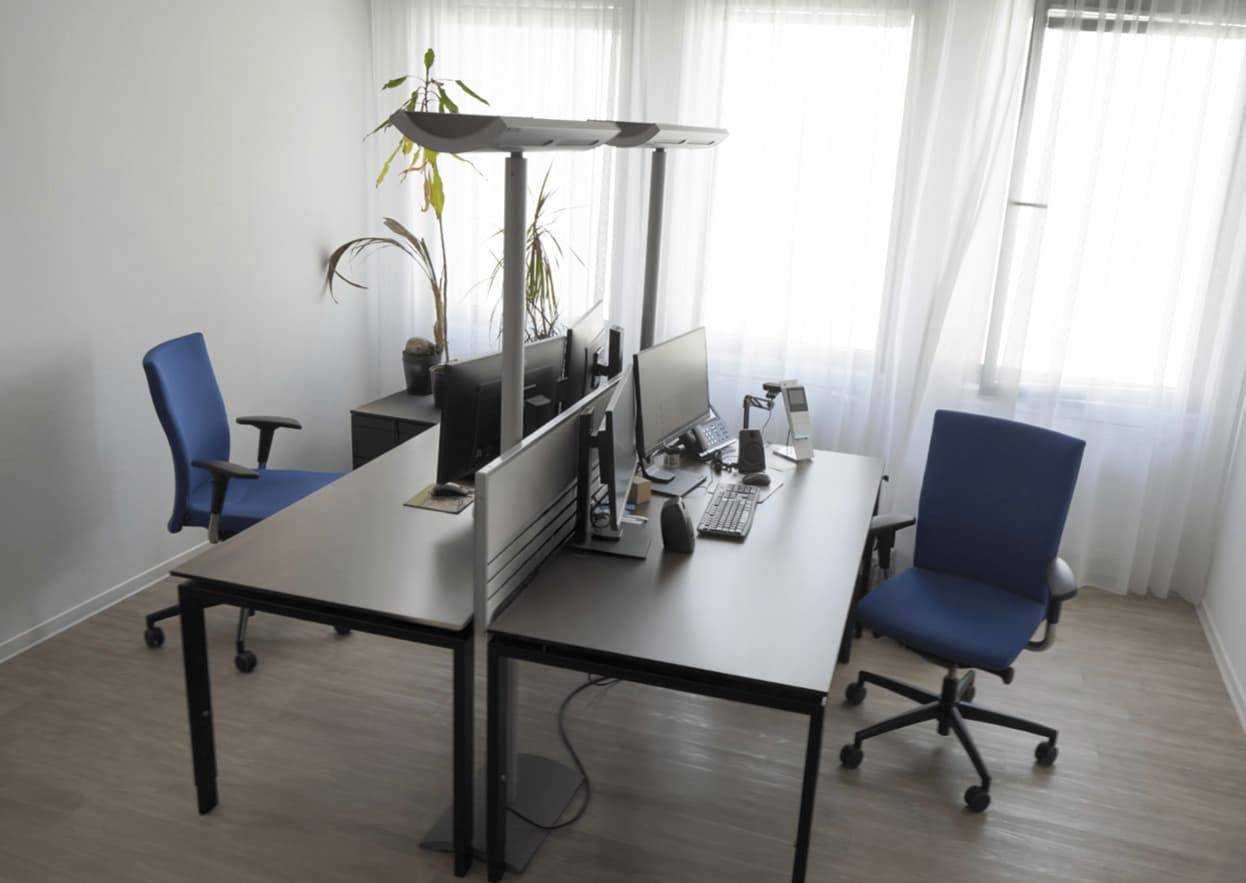 Modernes Großraumbüro mit mehreren Arbeitsplätzen, Computern und viel Tageslicht durch große Fenster.