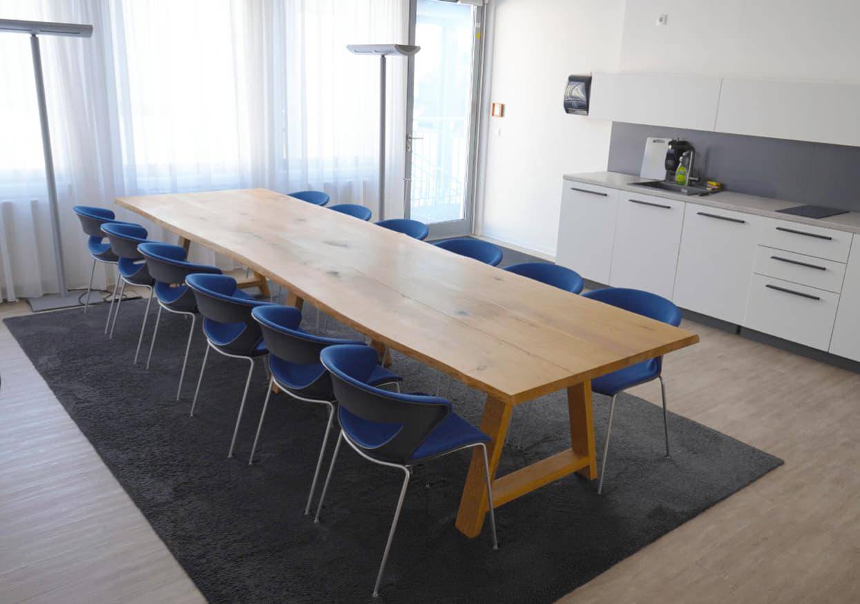 Großer Konferenzraum mit langem Holztisch, blauen Stühlen und integrierter Küchenzeile für Besprechungen.