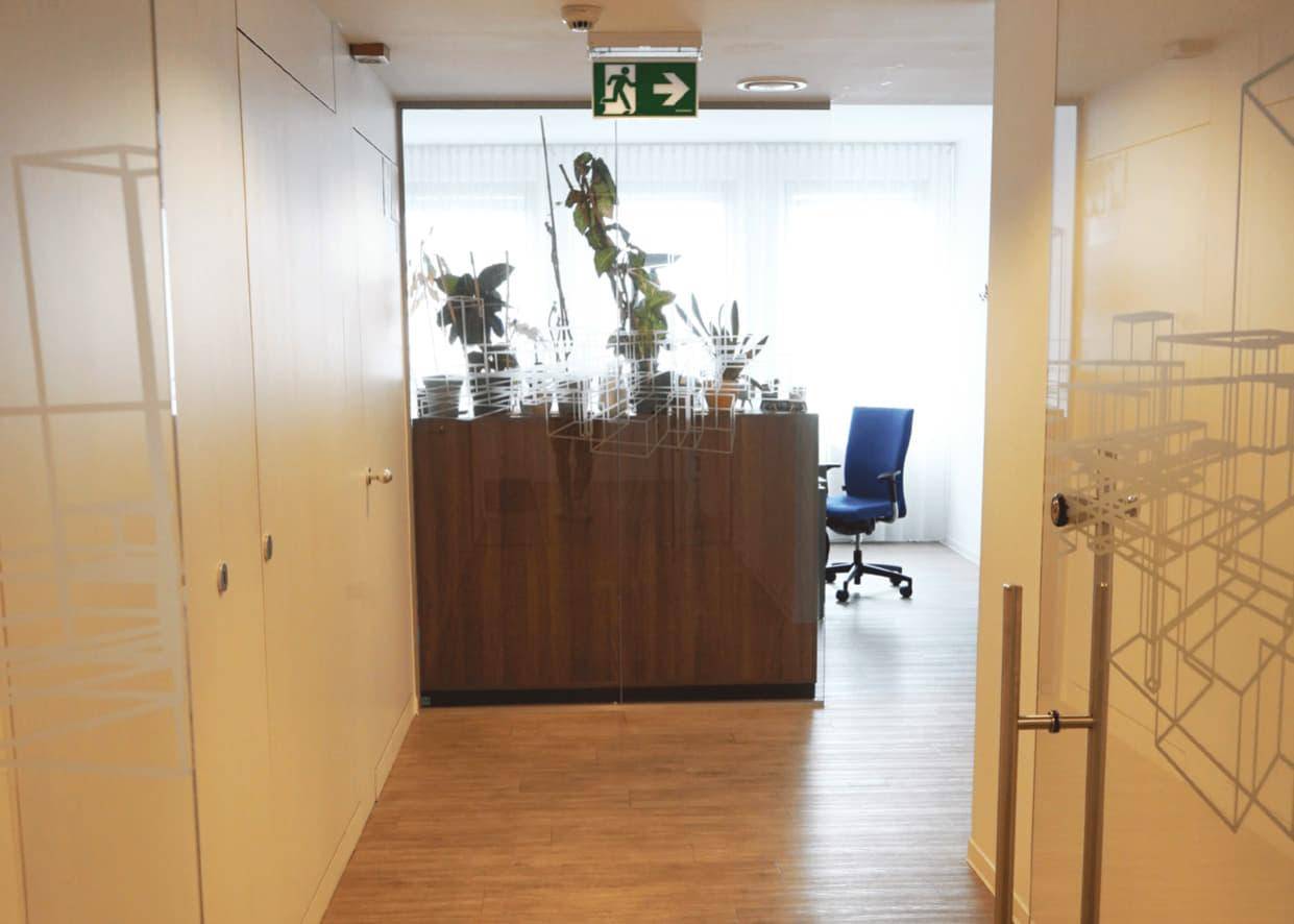Heller Flur mit Holzboden und Glaswänden, der zu einem modernen Bürobereich führt.