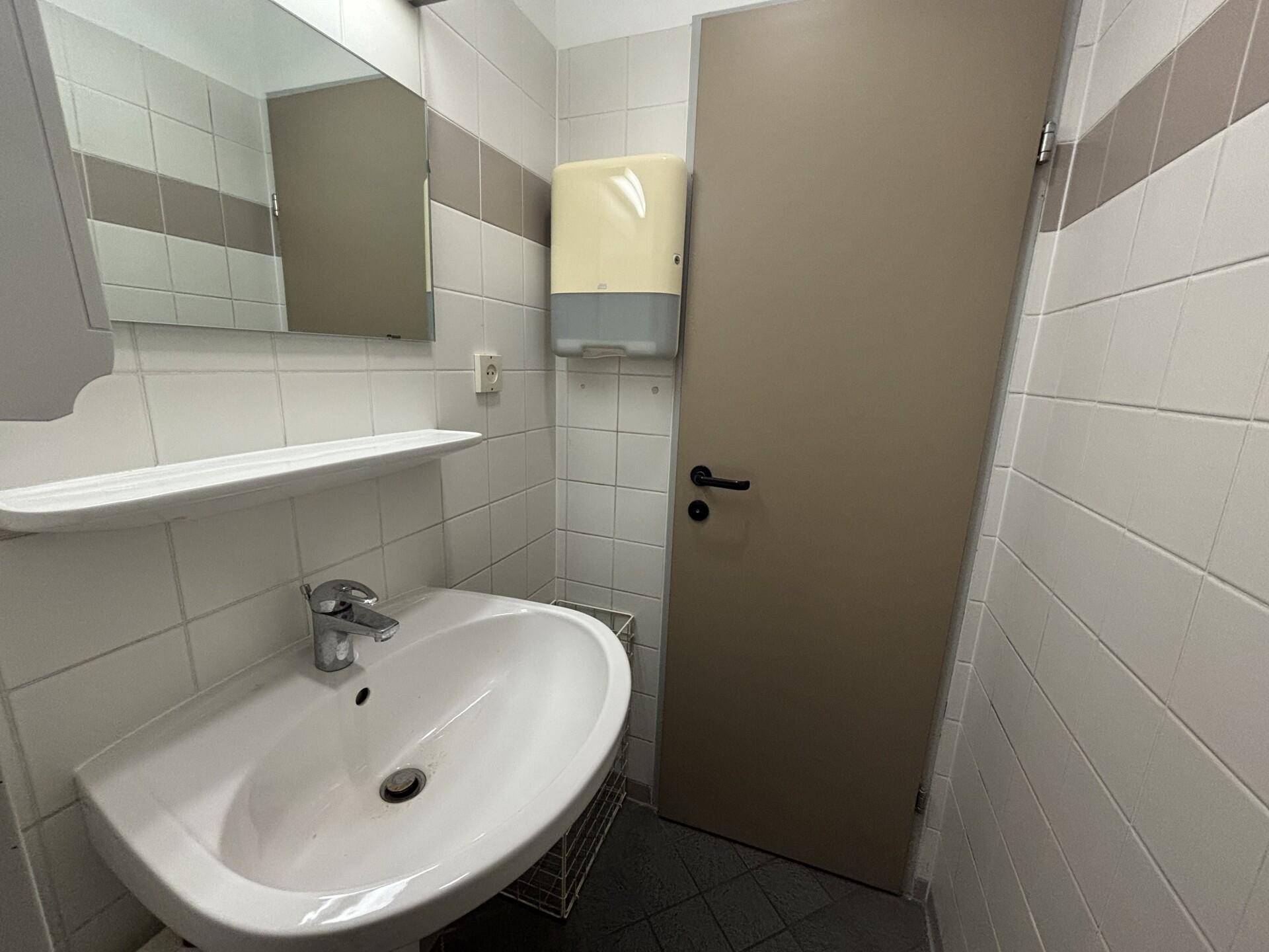 Saubere Toilette mit weißen Fliesen, Waschbecken und einem Spiegel.