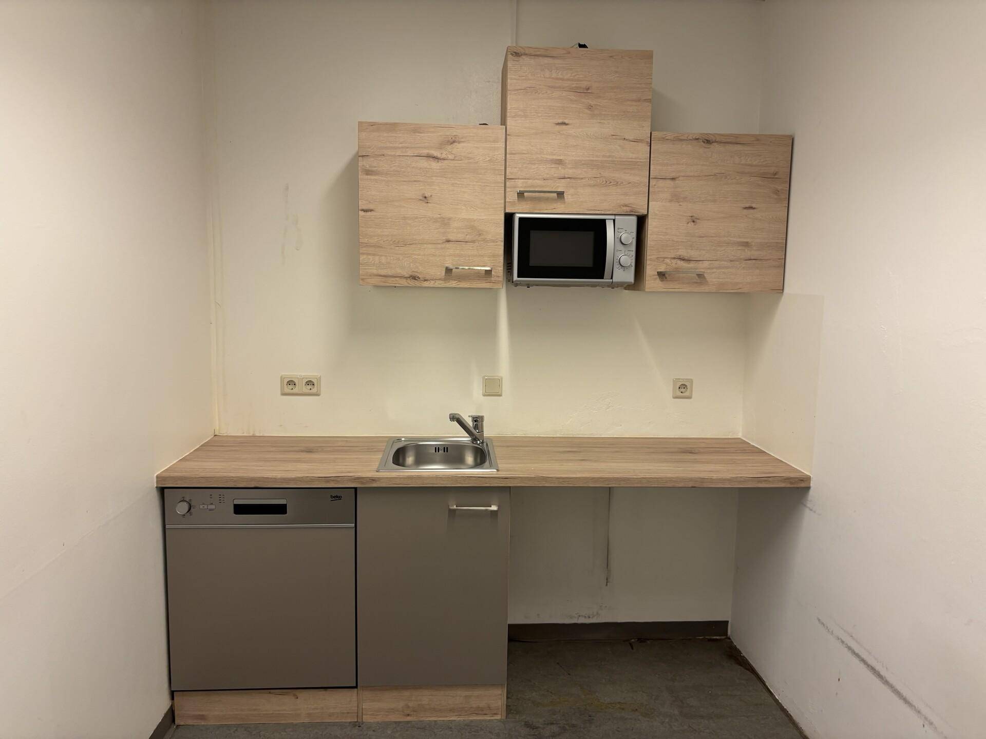 Kleine Küchenzeile mit Holz-Arbeitsplatte, Spüle, Mikrowelle und integriertem Geschirrspüler.