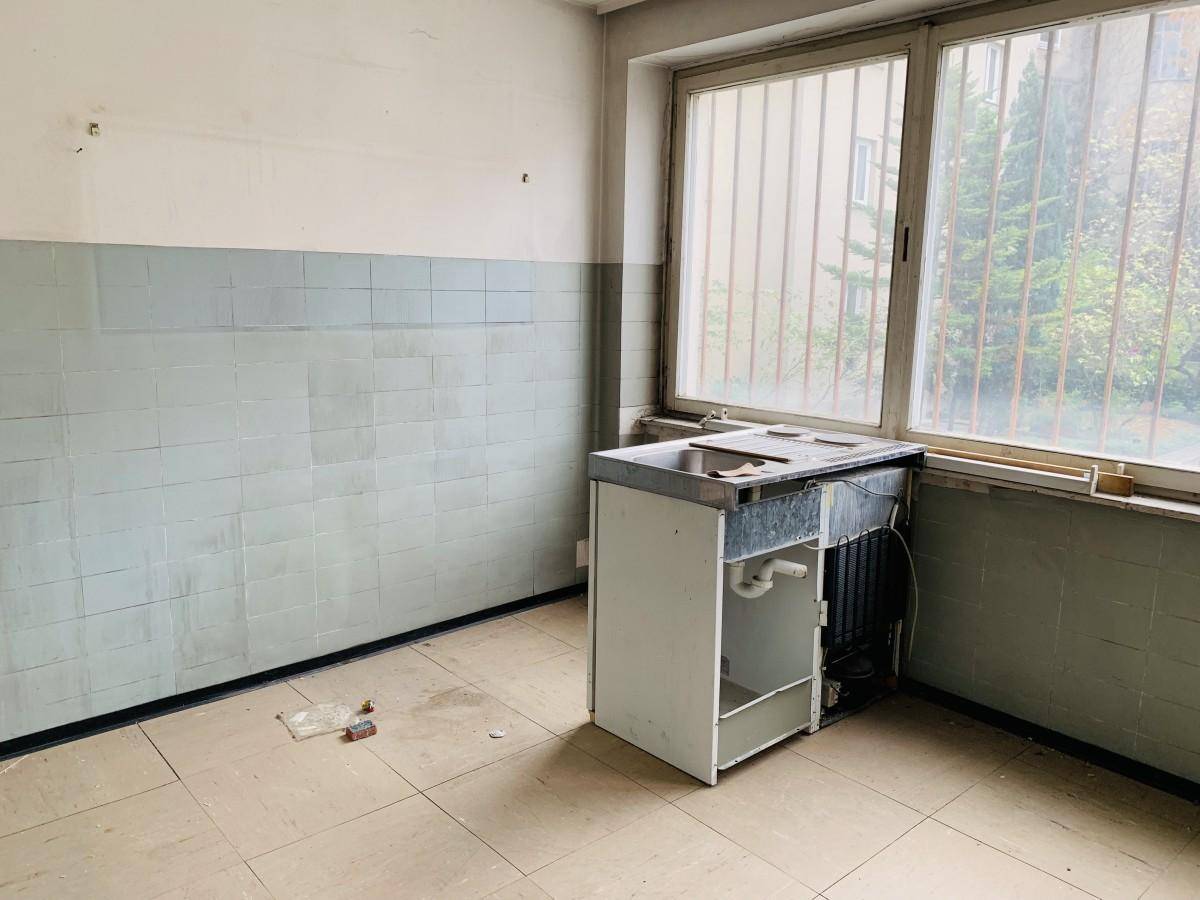 Einfacher Raum mit Waschbecken, Fliesenwänden und Fenster, renovierungsbedürftig.