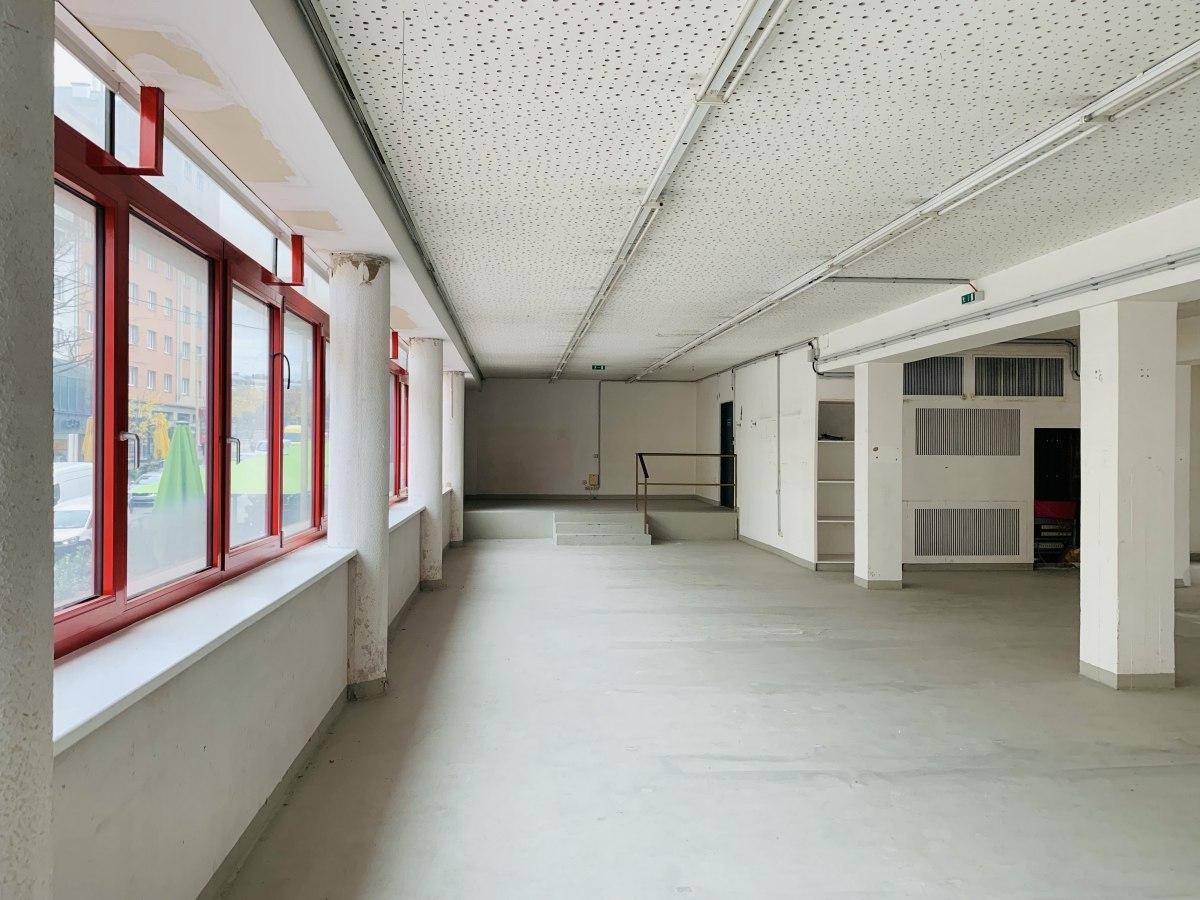 Heller Gewerberaum mit roten Fensterrahmen und strukturierten Deckenplatten.