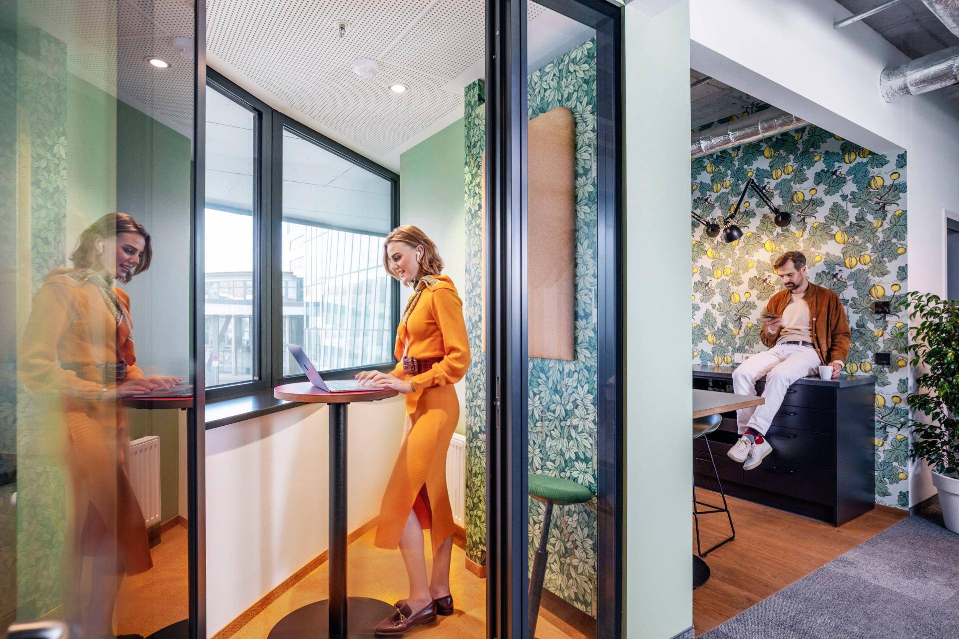 Kreative Büroumgebung mit privater Arbeitskabine und offenem Bereich mit gemusterter Tapete.
