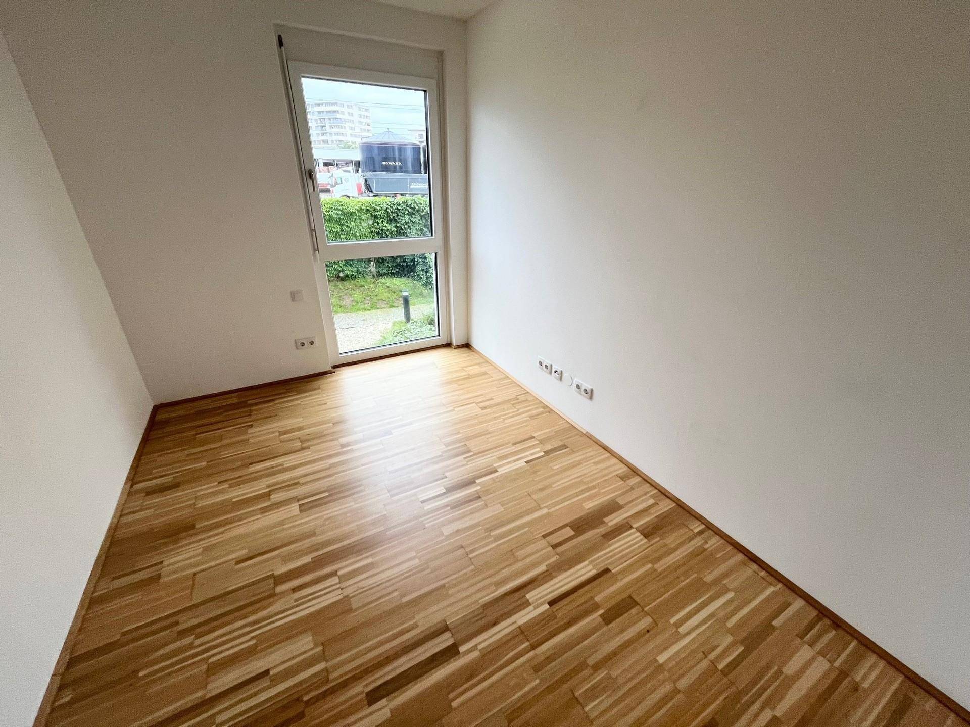 Weiteres helles Zimmer mit Parkettboden und Fenster, das viel Tageslicht hereinlässt.