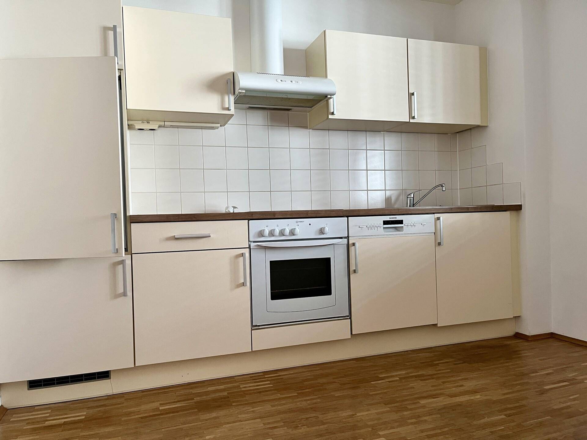 Einbauküche in hellem Beige mit Holz-Arbeitsplatte, Spülmaschine und Backofen.