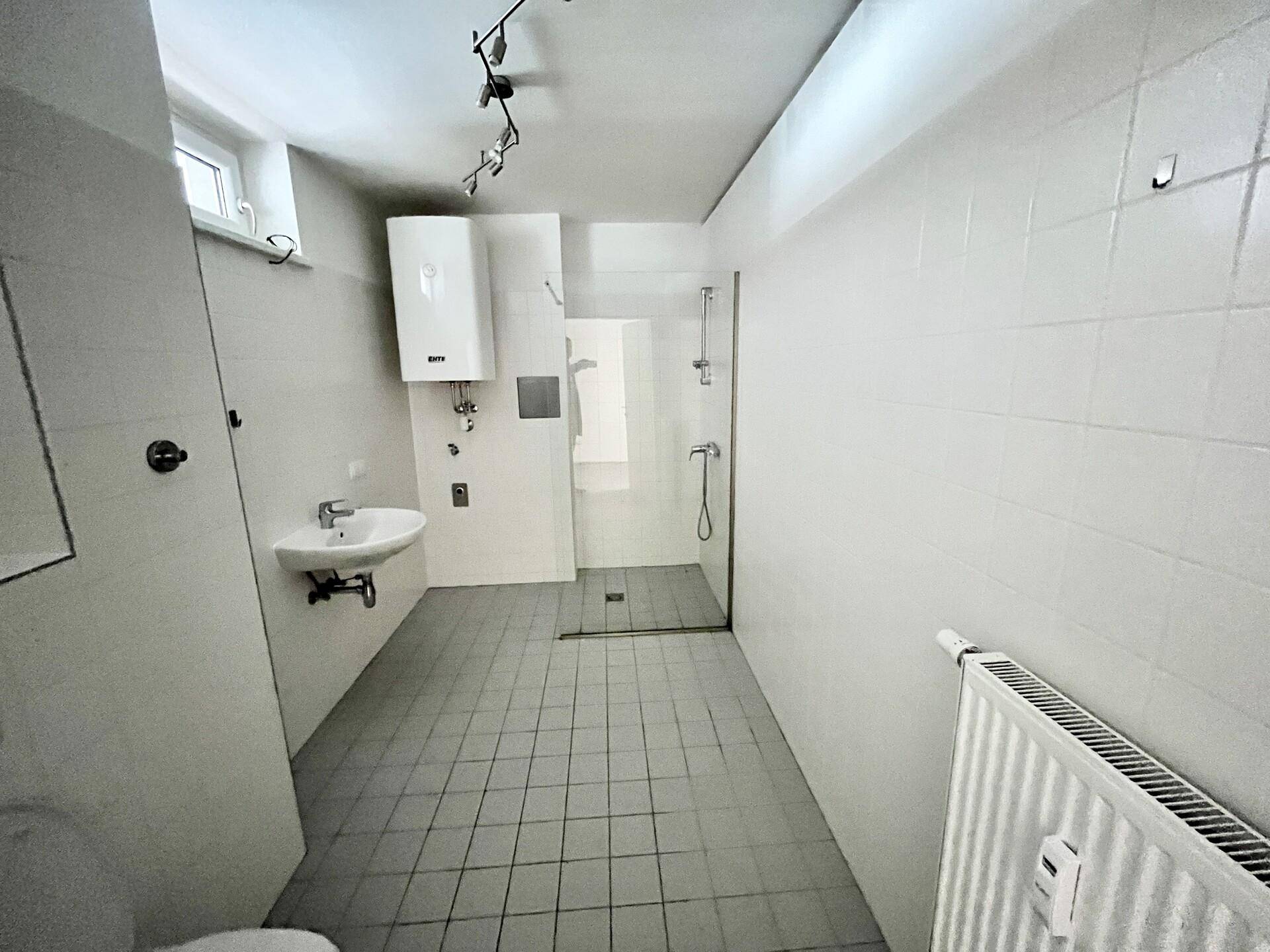 Funktionales Badezimmer mit Fliesenboden, Dusche und Fenster für natürliche Belüftung.