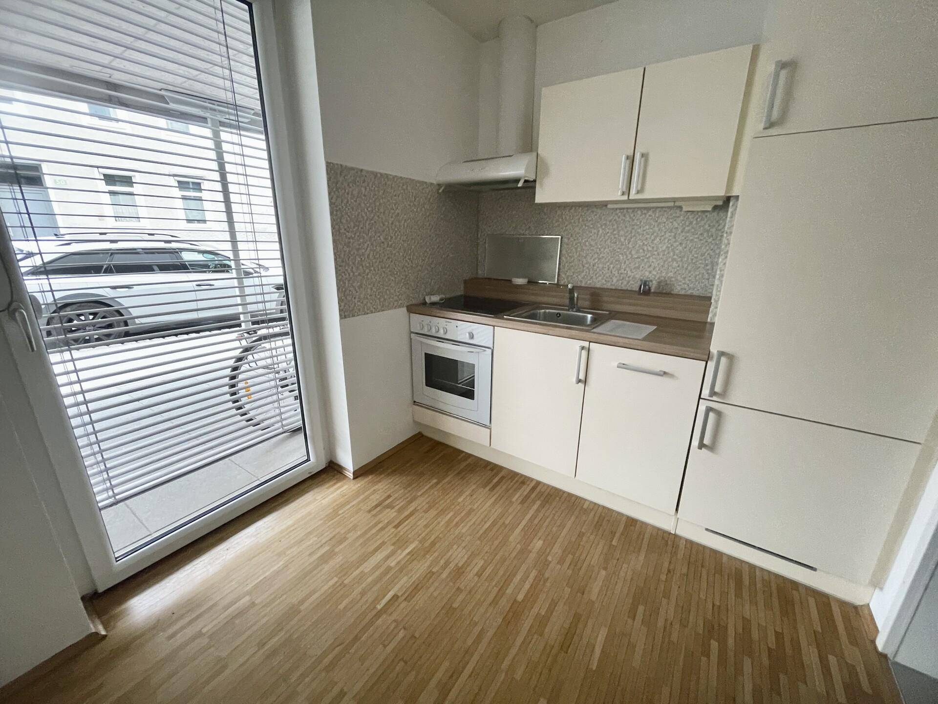 Kleine Einbauküche mit hellen Schränken, Herd und Kühlschrank sowie Zugang nach draußen.