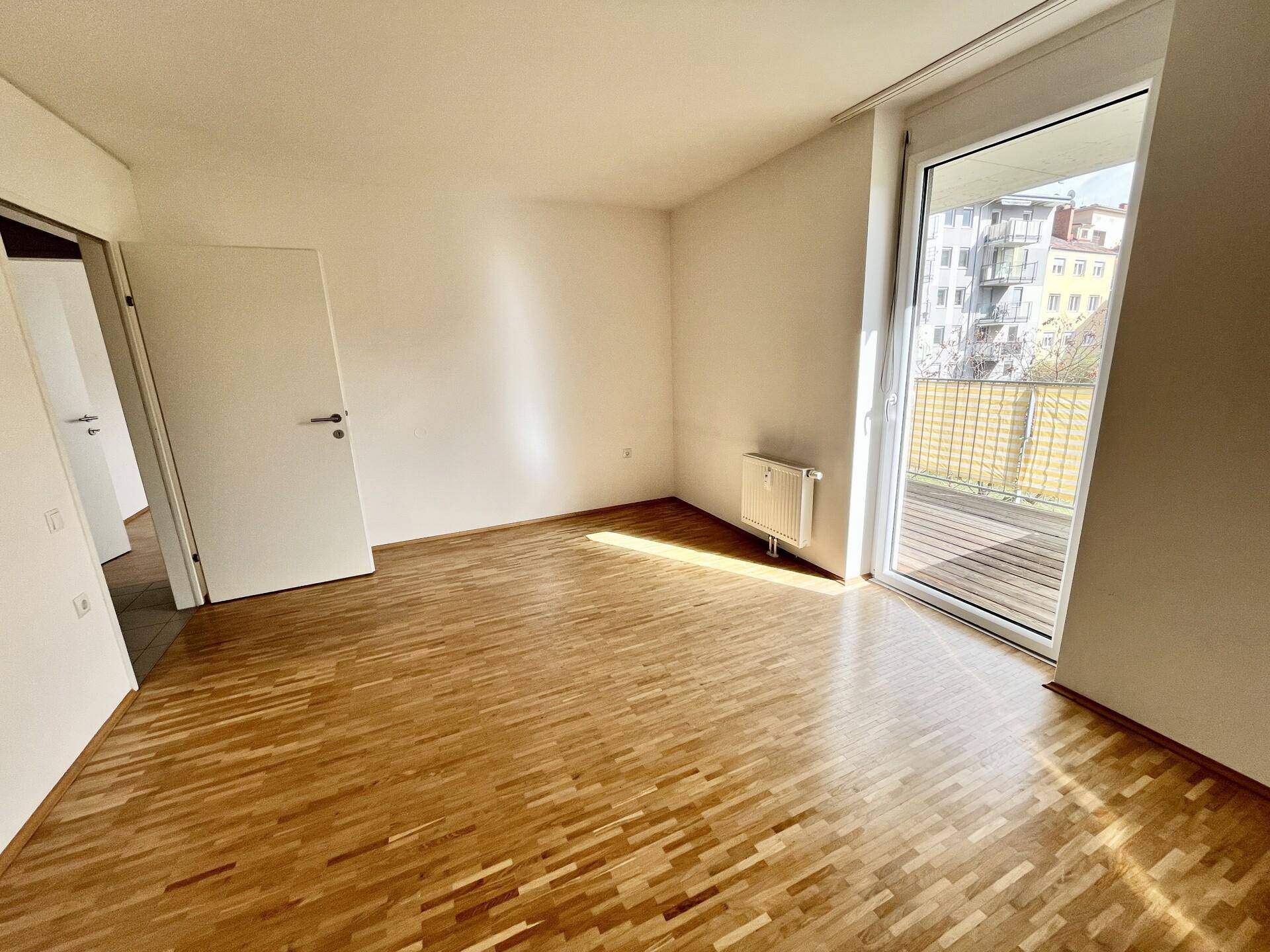 Heller Raum mit Parkettboden und Zugang zu einem Balkon, ideal als Wohn- oder Schlafzimmer.