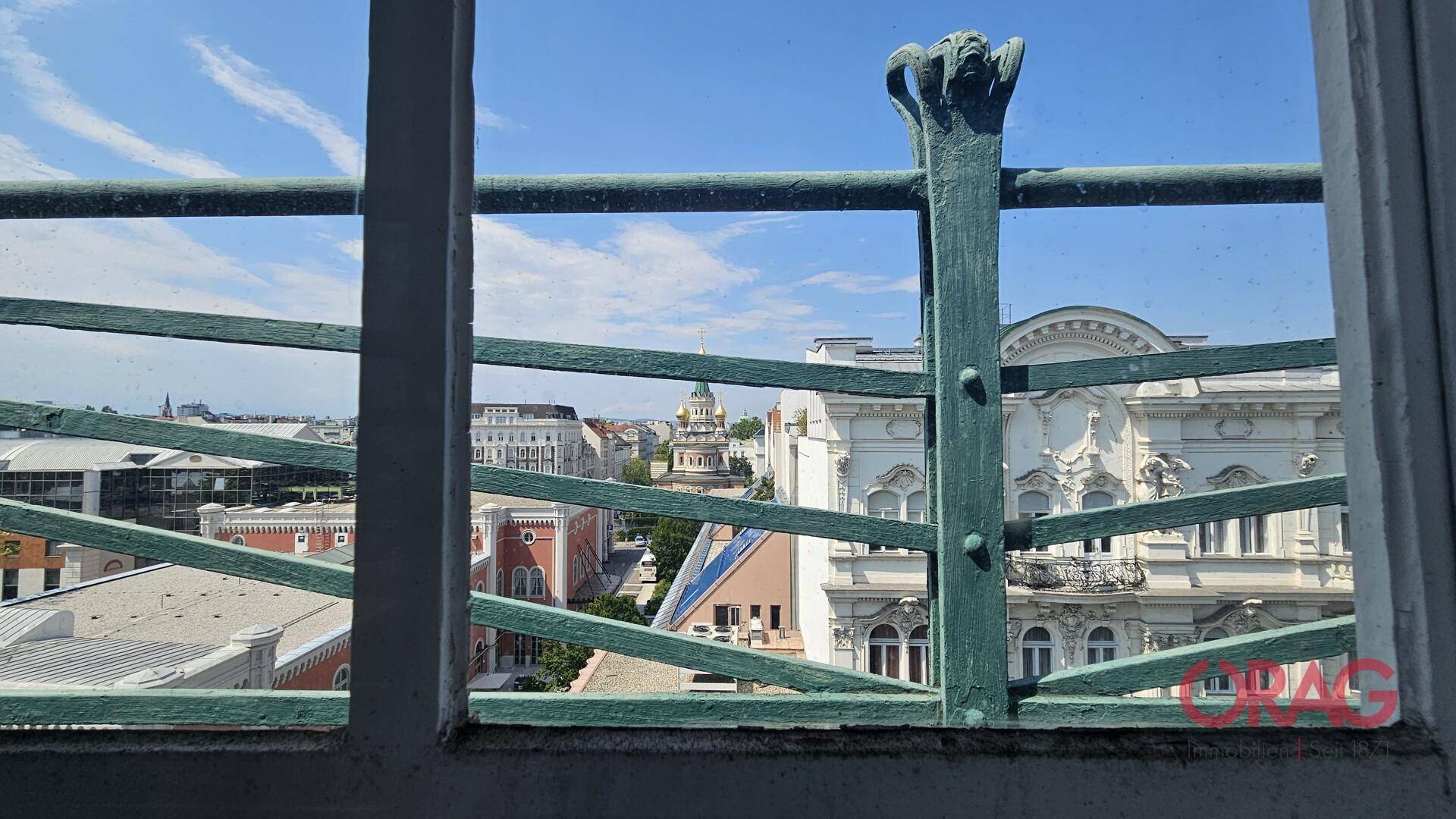 Panoramablick auf die Stadt durch ein kunstvolles Fenstergitter, das historische Gebäude zeigt.