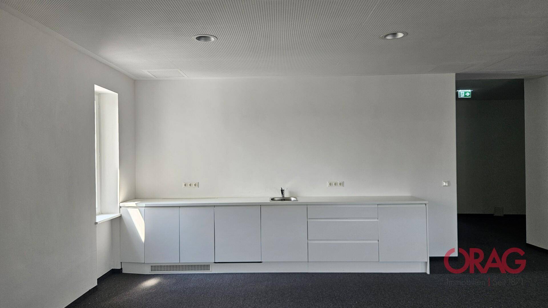 Kleine, moderne Küchenzeile mit weißen Schränken und Spüle, ideal für eine Büropause.