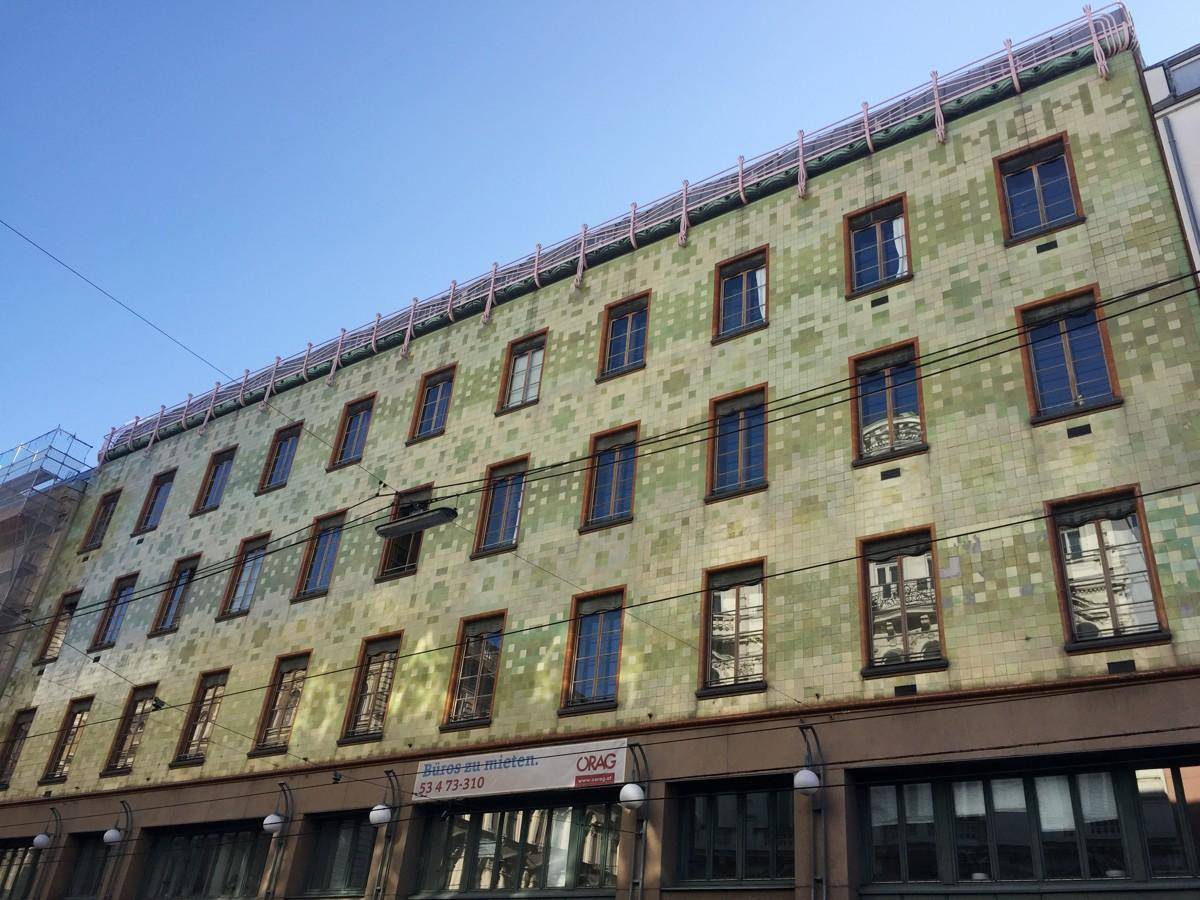 Historische Gebäudefassade mit charakteristischen grünen Kacheln und vielen Fenstern unter klarem Himmel.