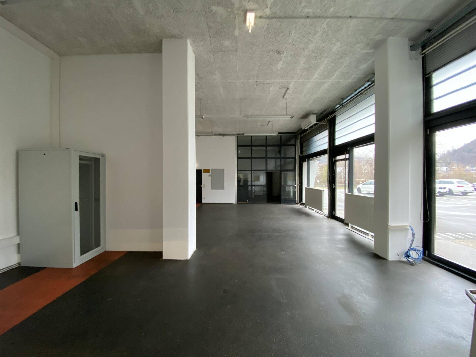 Geräumiger Gewerberaum mit großen Fenstern und Blick auf den Parkplatz, ideal für verschiedene Nutzungen.