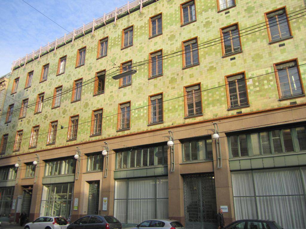 Historisches Gebäude mit auffälliger grüner Kachelfassade und traditionellen Holzfenstern in urbaner Umgebung.