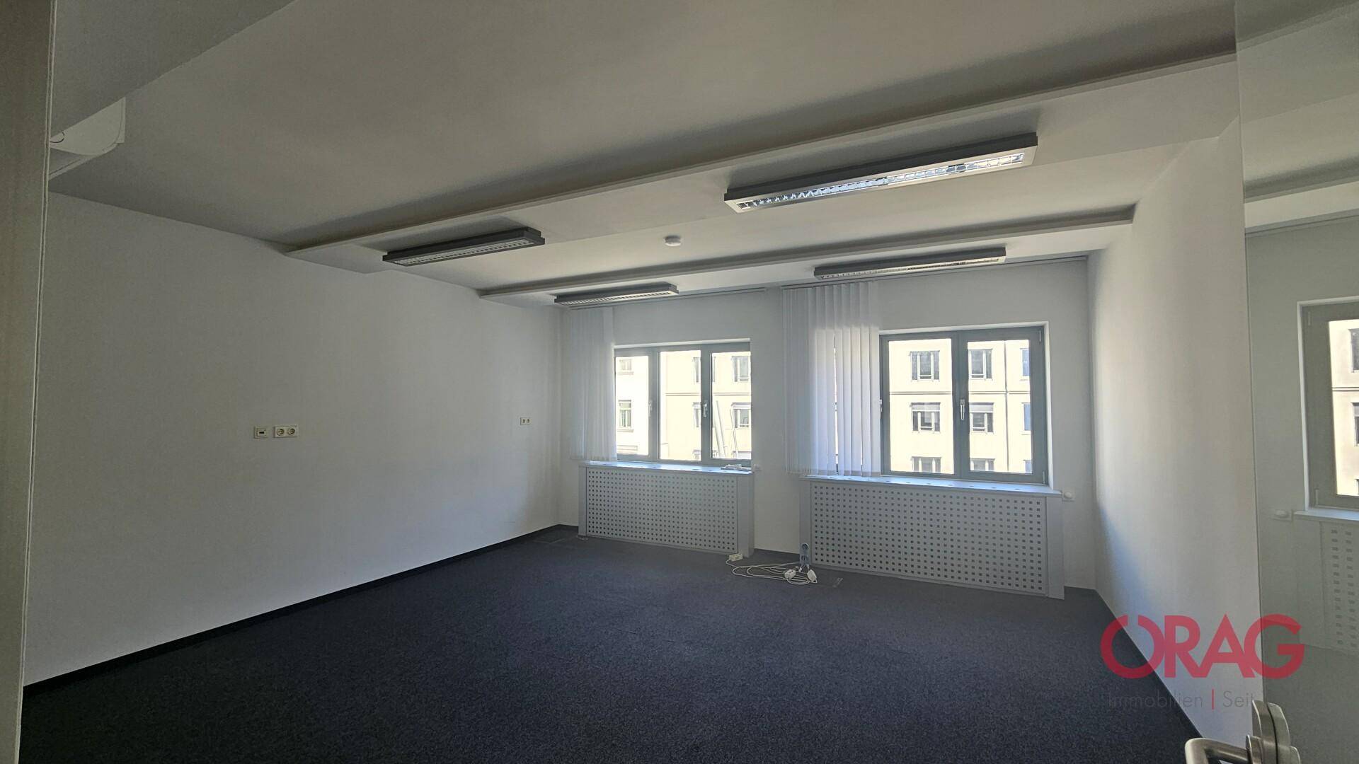 Helles Büro mit Teppichboden, großen Fenstern und Jalousien, bereit für die Büroeinrichtung.