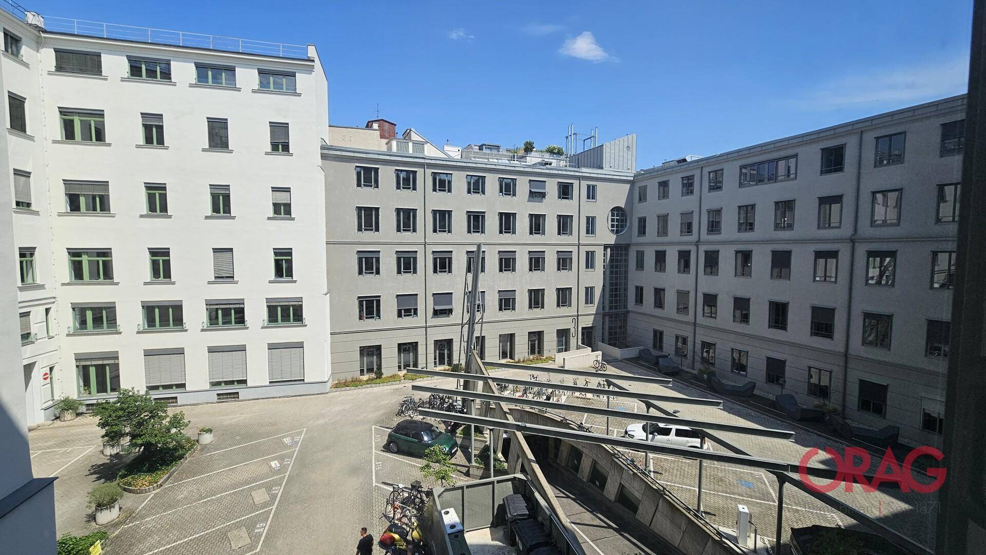 Innenhofansicht eines Gebäudekomplexes mit Parkplätzen und Fahrradständern unter blauem Himmel.