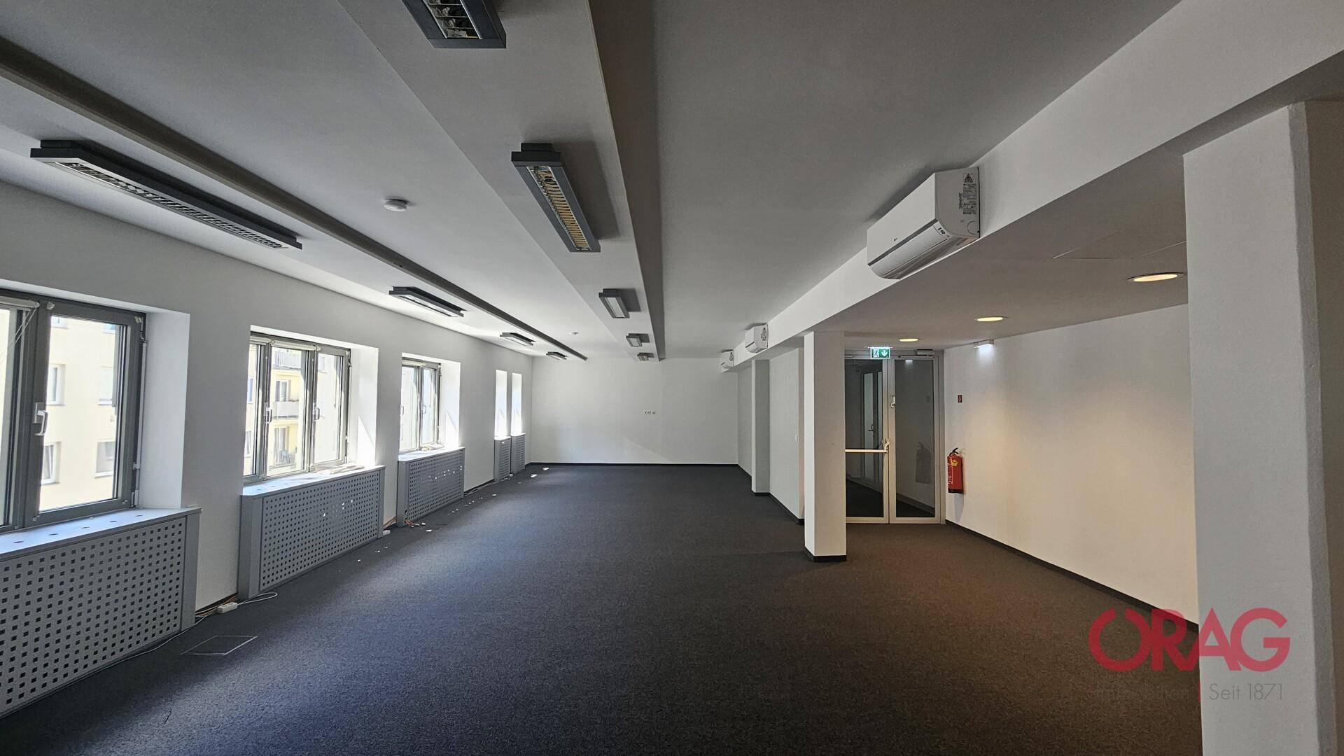 Großes, leeres Büro mit Teppichboden, Klimaanlage und Fenstern, die viel Tageslicht hereinlassen.