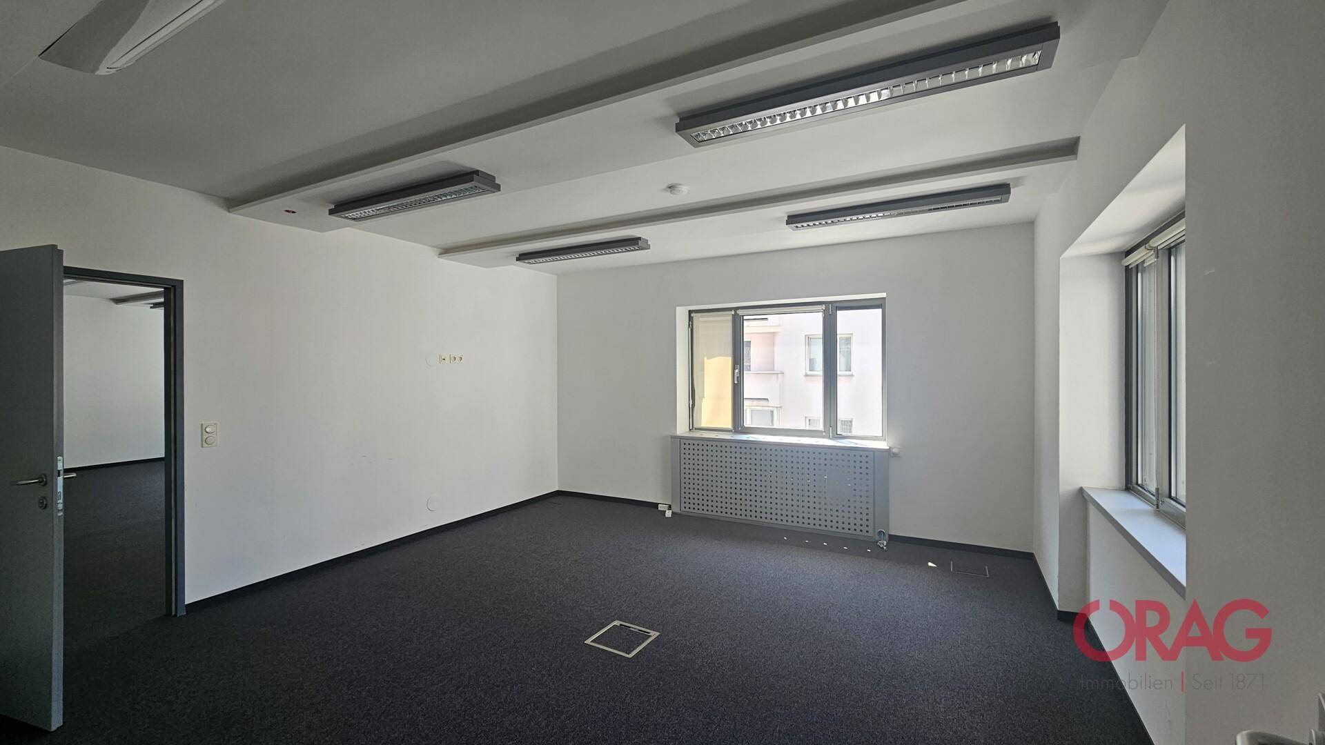 Helles Büro mit Teppichboden, großen Fenstern und Heizkörpern, bereit zur individuellen Gestaltung.