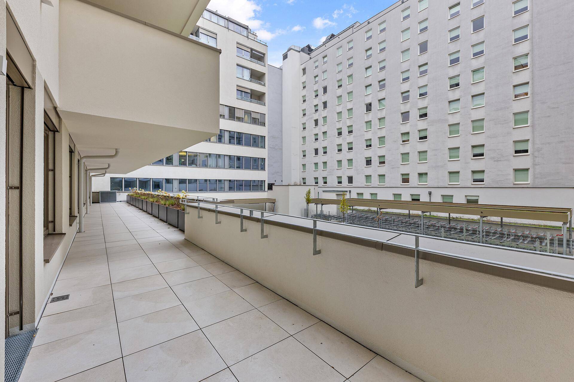 Weitläufige Außenterrasse mit Fliesenboden und Blick auf umliegende moderne Gebäude.