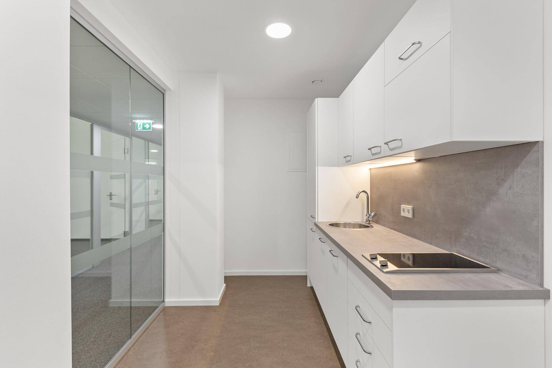 Moderne Küchenzeile mit weißen Schränken, Spüle und Kochfeld, ideal für eine Büroküche oder Teeküche.