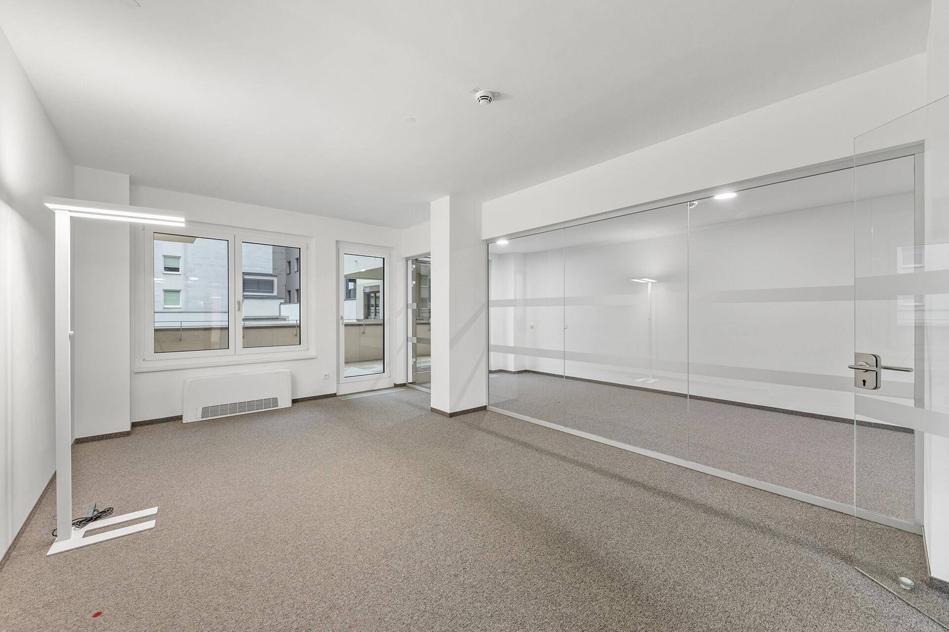 Helles Büro mit Teppichboden, großen Fenstern und Zugang zu einem Balkon, ideal für flexible Nutzung.