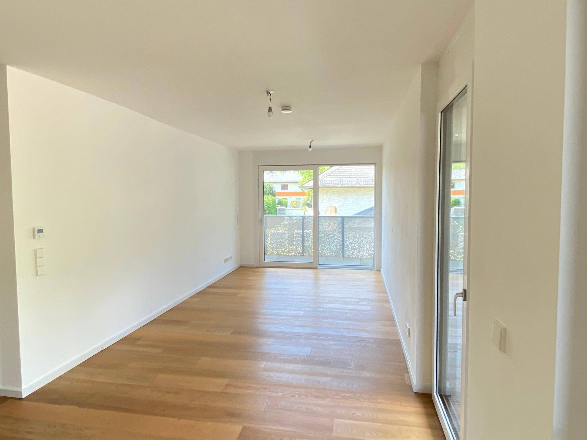Leeres, helles Zimmer mit Holzboden und großem Fenster, das zu einem Balkon führt.