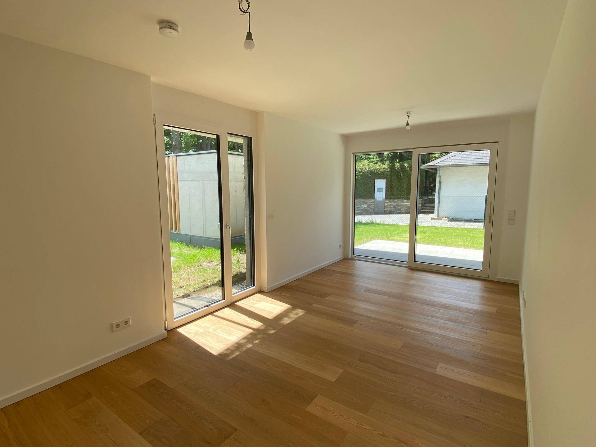 Heller, unmöblierter Raum mit Holzboden und großen Glasschiebetüren zum Gartenbereich.