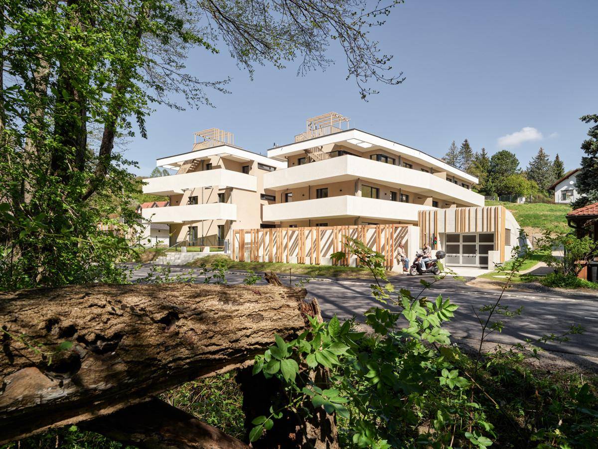 Modernes Mehrfamilienhaus mit mehreren Balkonen, umgeben von Bäumen und Grünflächen.