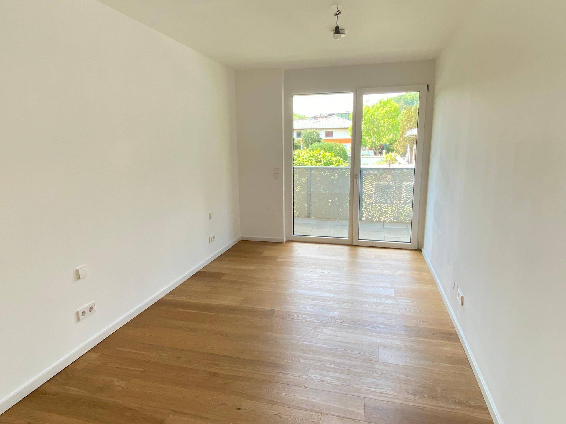 Helles, leeres Zimmer mit Holzboden und Zugang zu einem Balkon, ideal als Schlafzimmer.
