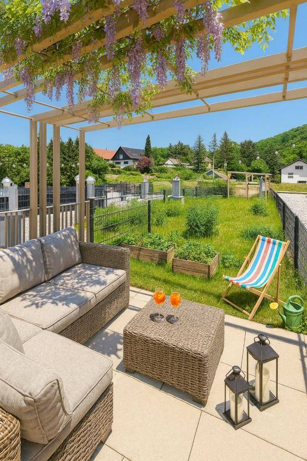 Idyllische Terrasse mit Pergola, Gartenmöbeln und Zugang zu einem kleinen Garten mit Hochbeeten.