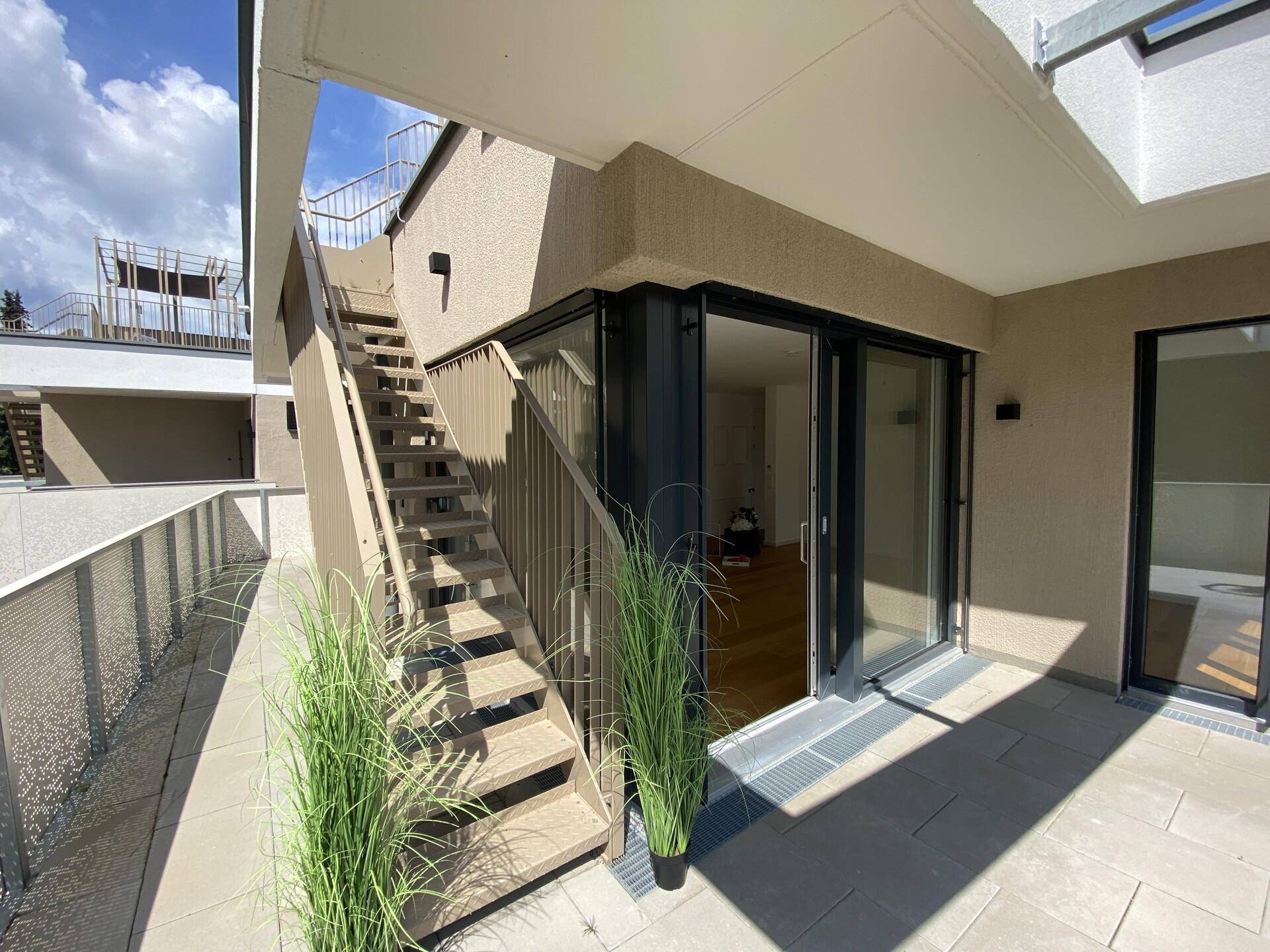 Außenansicht des Gebäudes mit einer Treppe, die zu den oberen Etagen führt, und Zugang zu einer Terrasse.