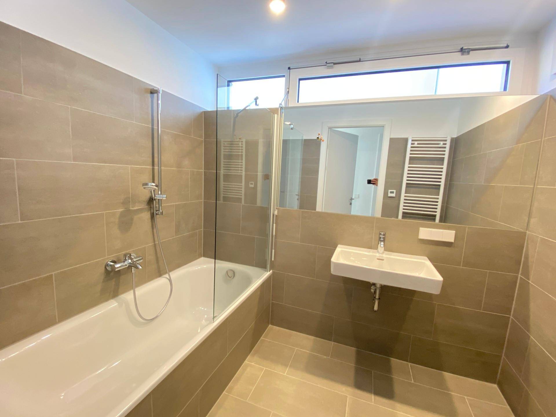 Modernes Badezimmer mit Badewanne, Duschabtrennung, Waschbecken und beheiztem Handtuchhalter.