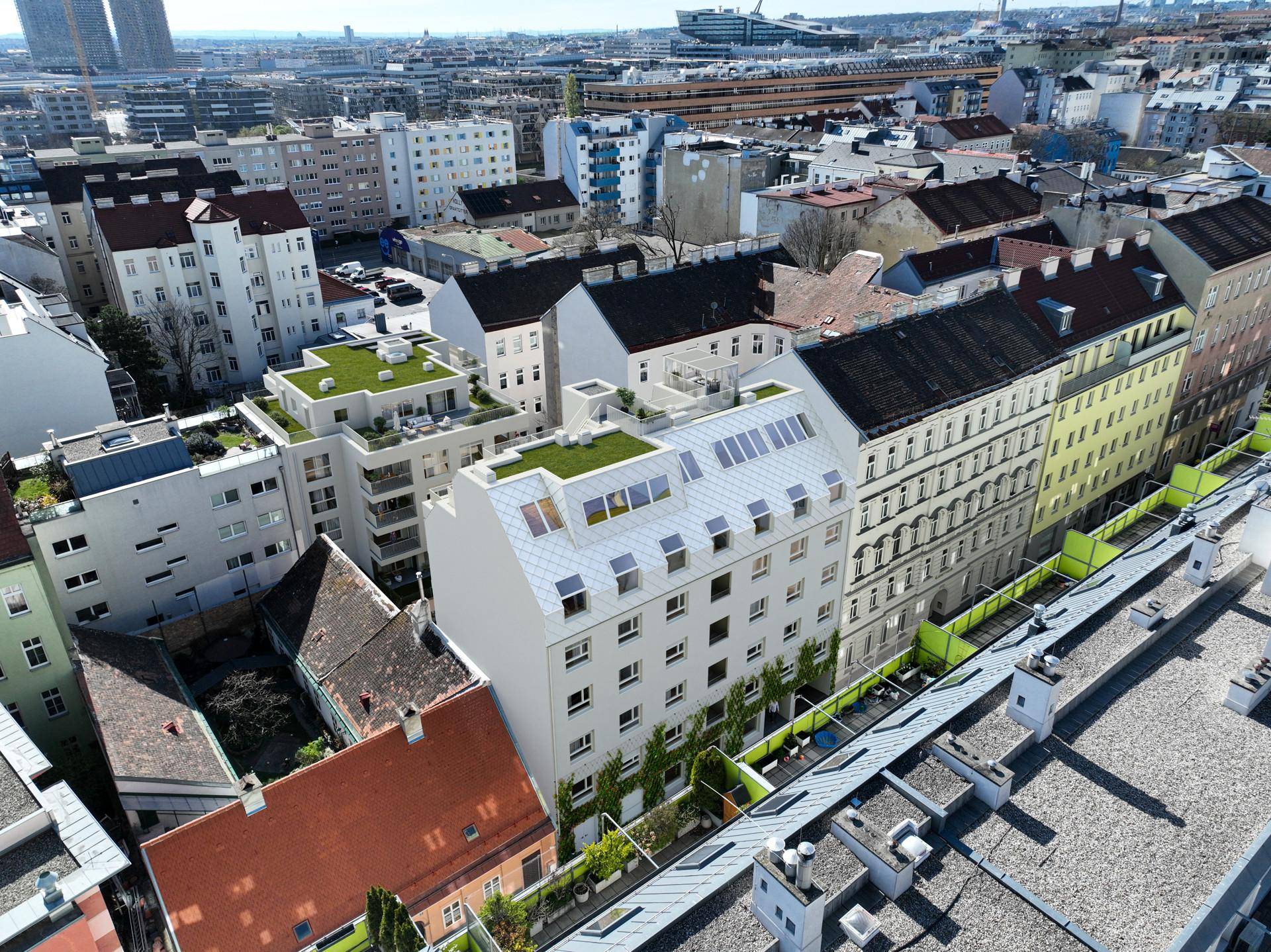 Luftaufnahme des modernen Neubaus in urbaner Umgebung mit begrünten Dächern und Altbauten.