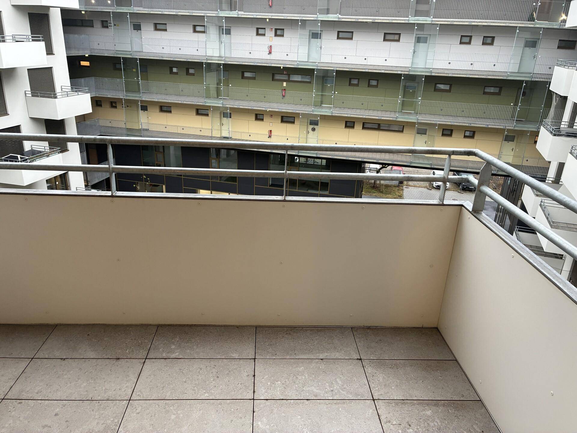 Balkon mit Fliesenboden und Blick auf den Innenhof des modernen Gebäudekomplexes.