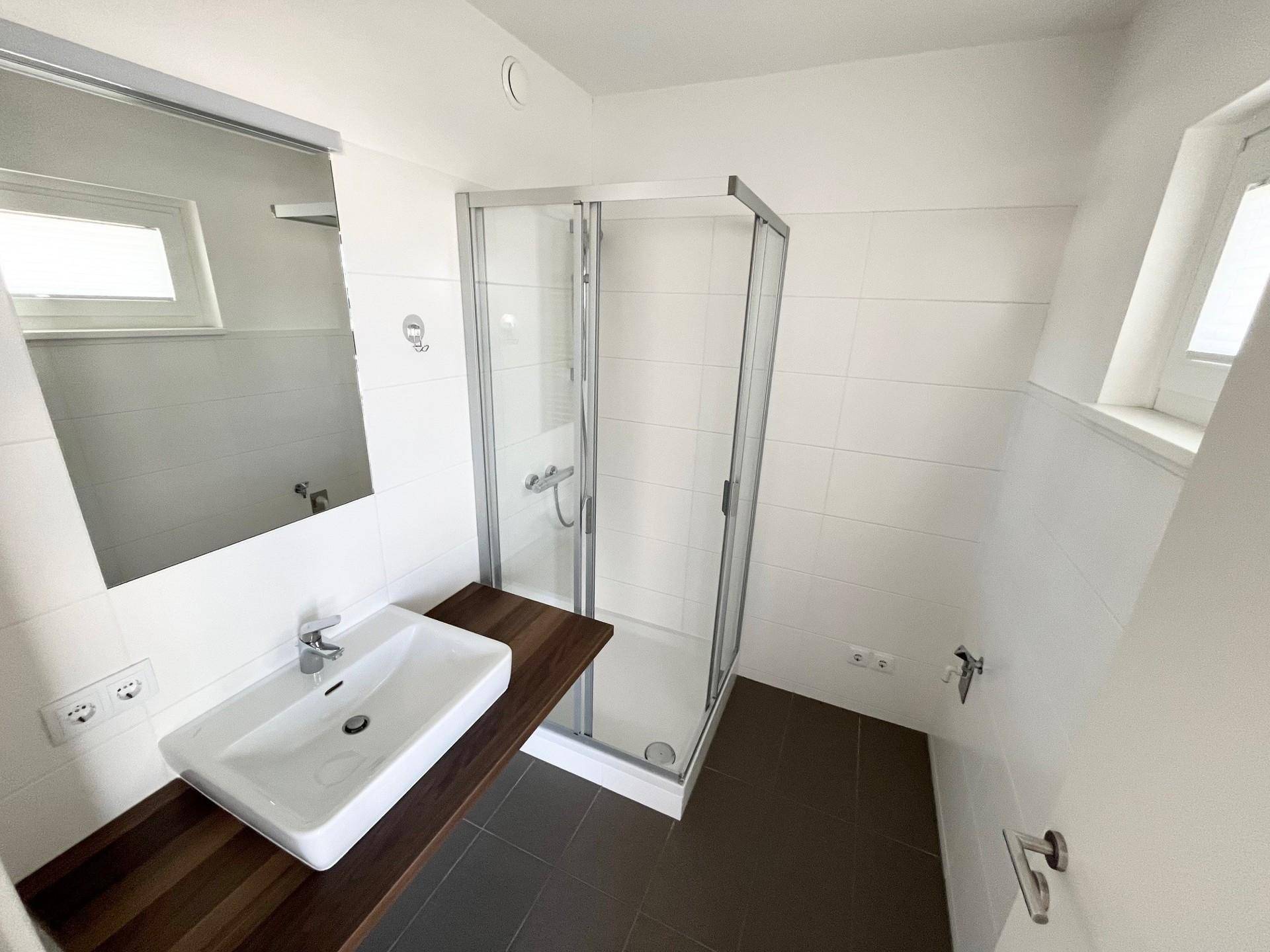 Modernes Badezimmer mit Duschkabine, Einzelwaschbecken und Fenster für Tageslicht.