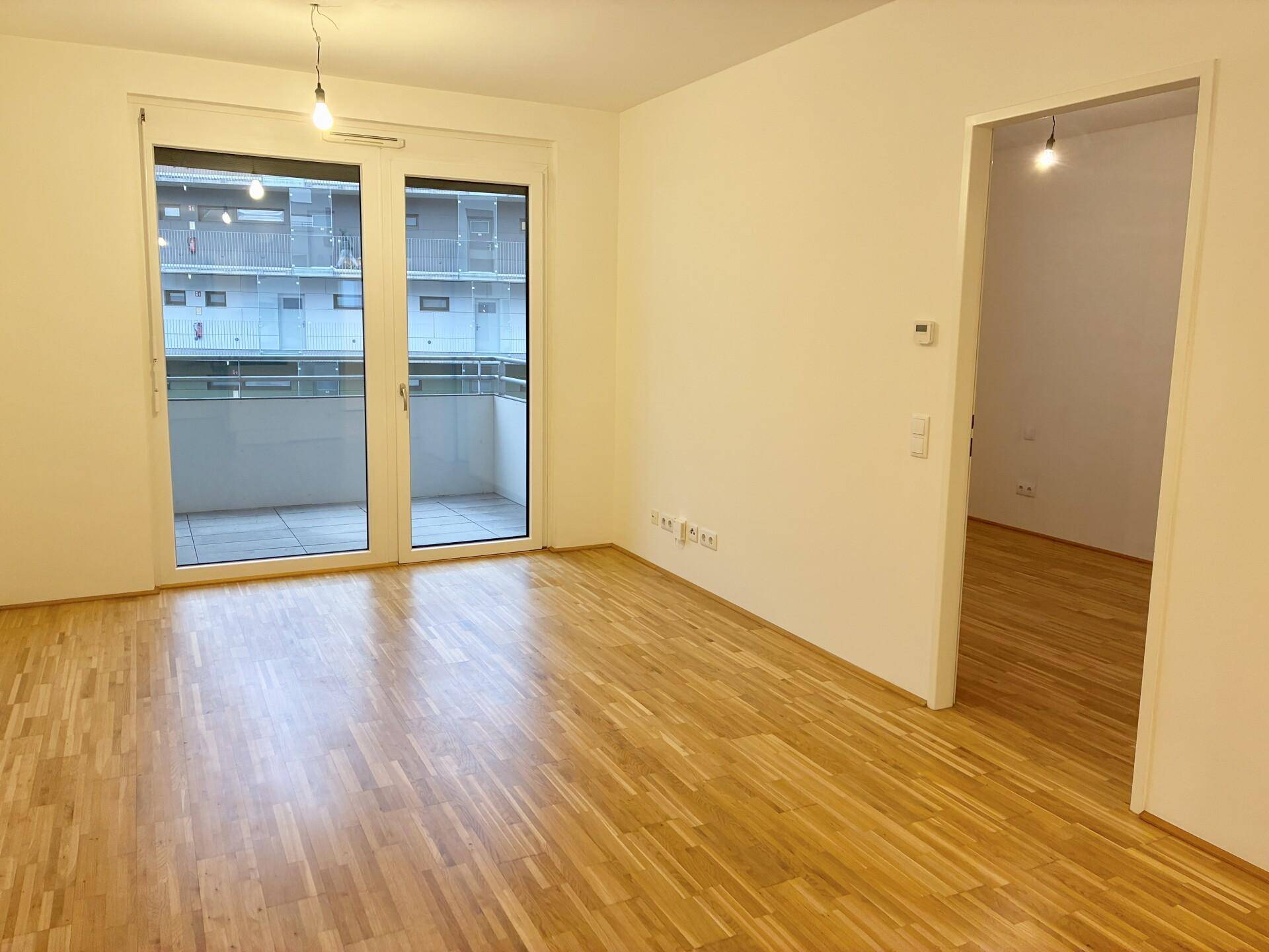 Geräumiges Zimmer mit Parkettboden und Zugang zu einem Balkon, ideal als Wohnbereich.