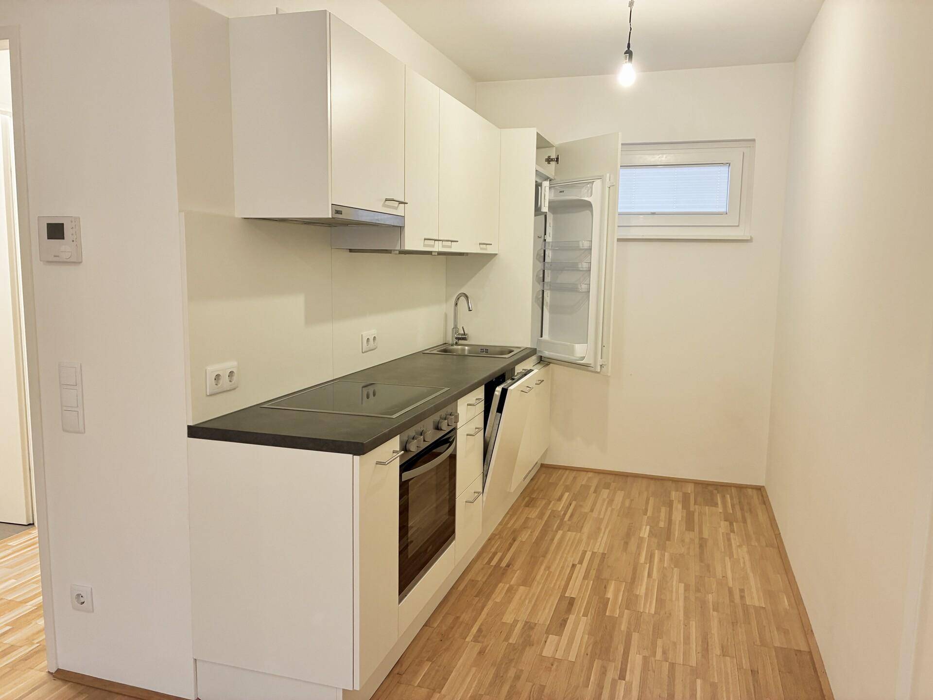 Moderne Einbauküche mit weißen Schränken, integrierten Geräten und Fenster.