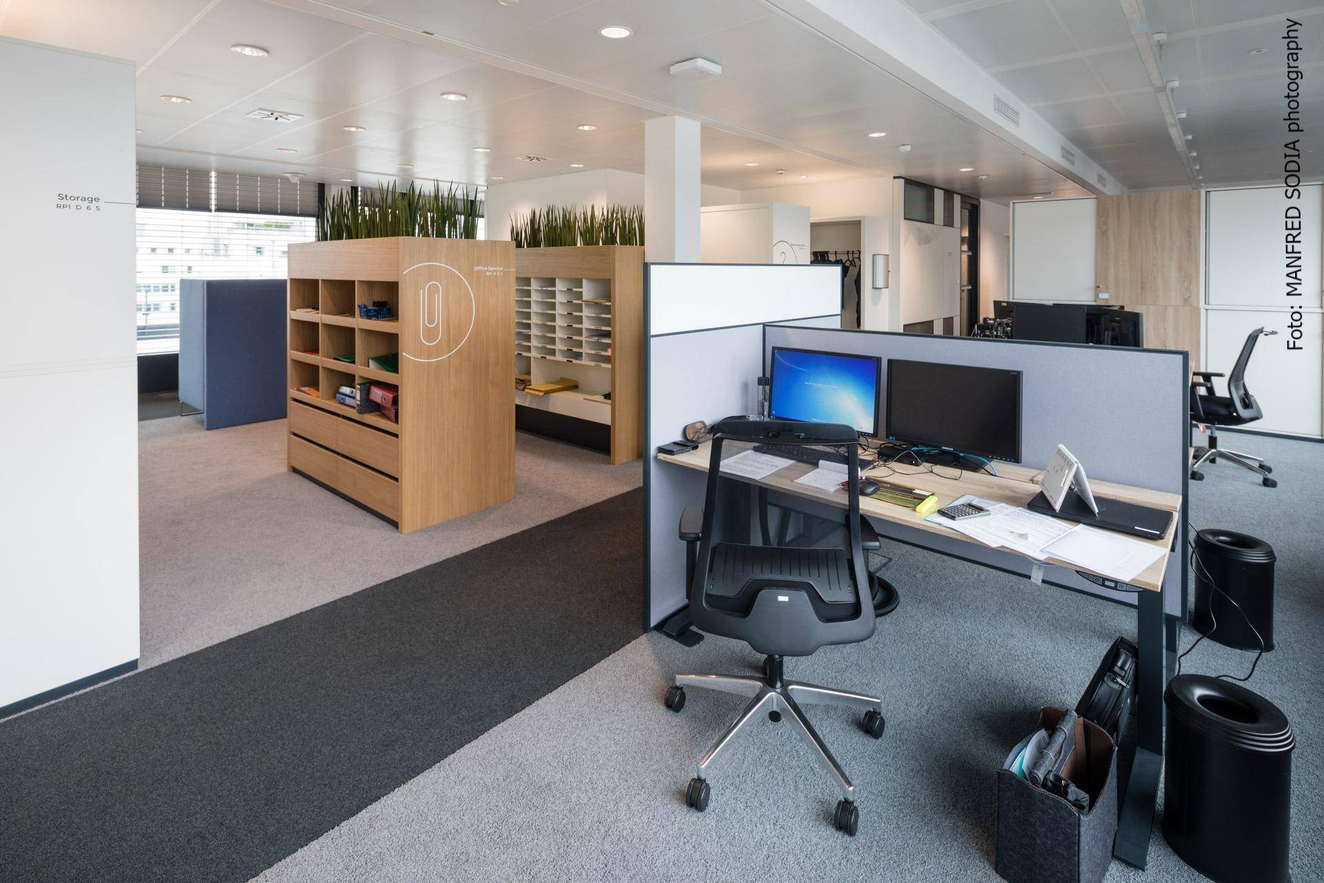 Offenes Büro mit modernen Arbeitsplätzen, Computern und integrierten Stauraummöbeln.