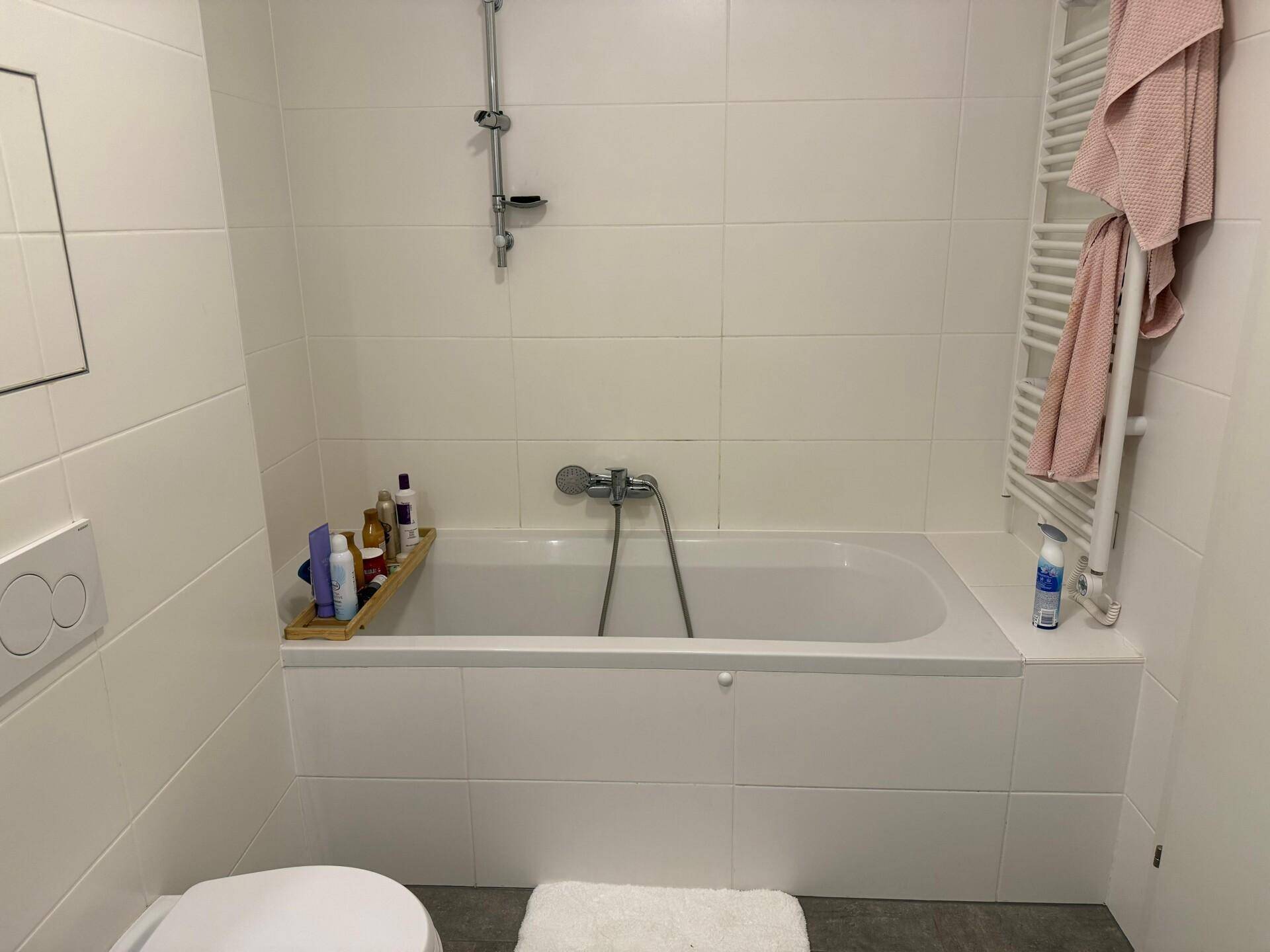 Helles Badezimmer mit Badewanne, Duschvorrichtung und weiß gefliesten Wänden.