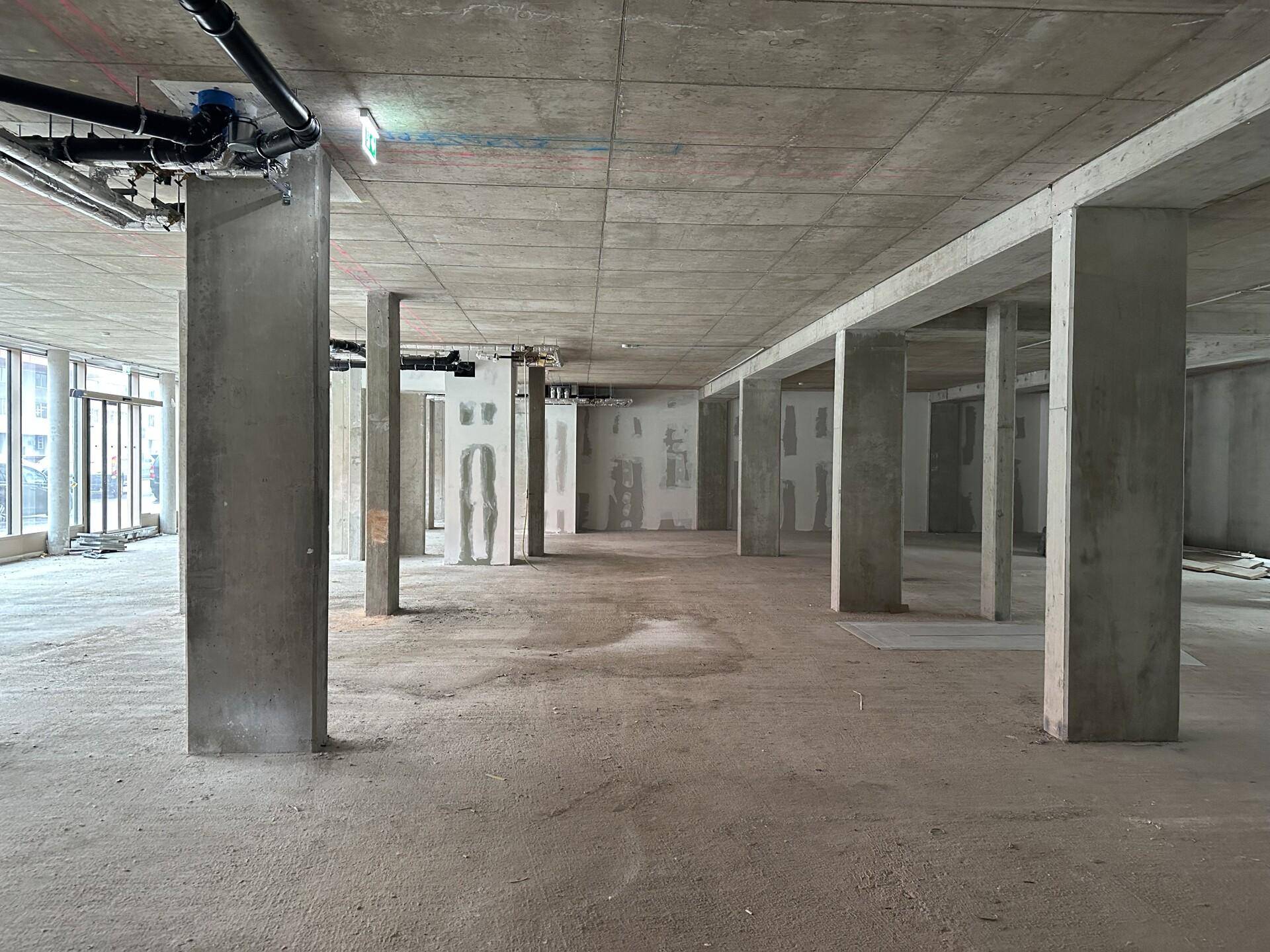 Großer, offener Rohbau-Raum mit Betonstützen und sichtbaren Installationen an der Decke.