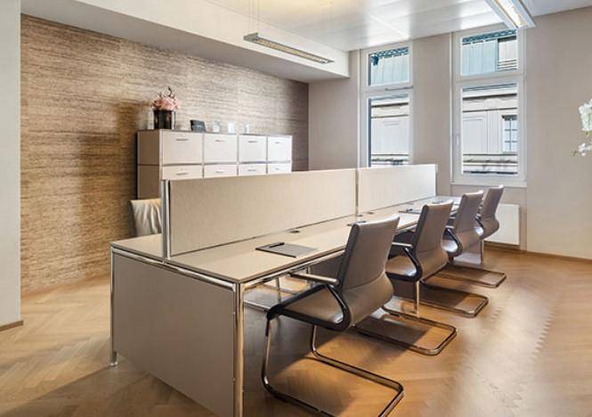 Helles und modernes Büro mit mehreren Arbeitsplätzen, großen Fenstern und Holzparkettboden.