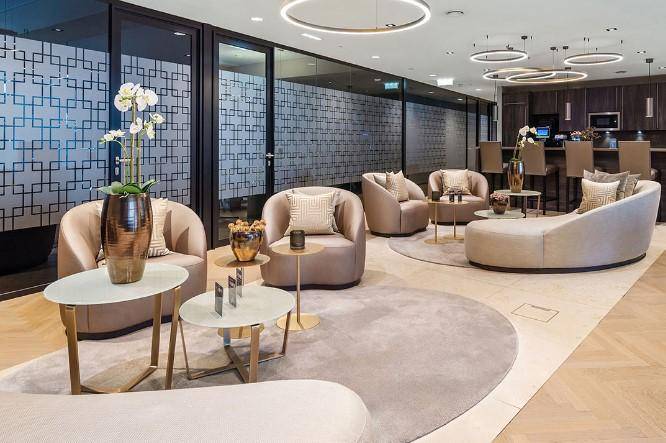 Geräumige und stilvolle Lounge mit verschiedenen Sitzbereichen, modernen Leuchten und einem Barbereich im Hintergrund.
