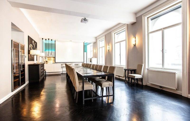 Großer Konferenzraum mit langem Tisch, vielen Stühlen, dunklem Parkett und Projektionsfläche für Präsentationen.