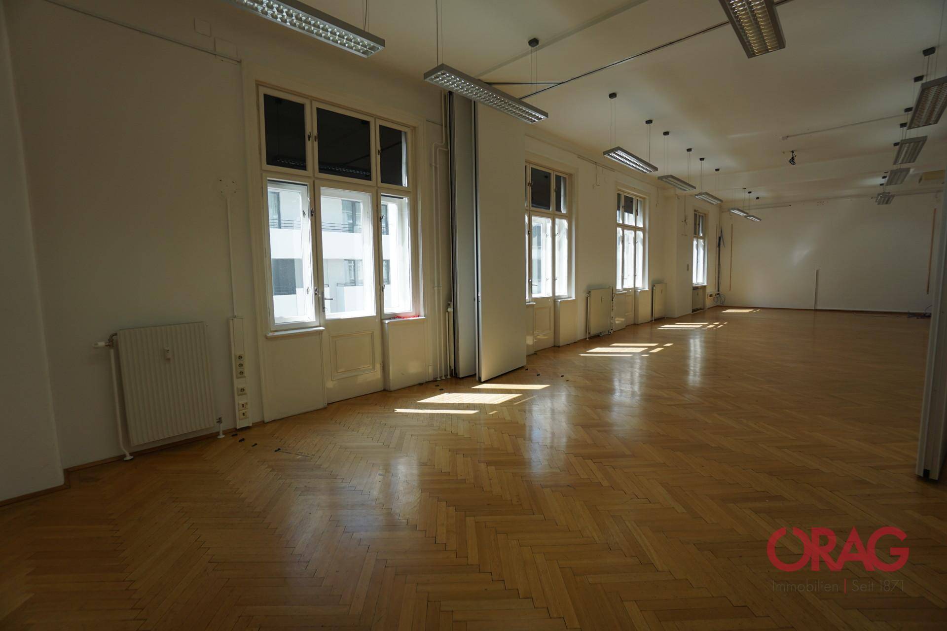 Geräumiger Büroraum mit Fischgrätparkett, hohen Fenstern und viel Tageslicht, ideal für flexible Nutzung.