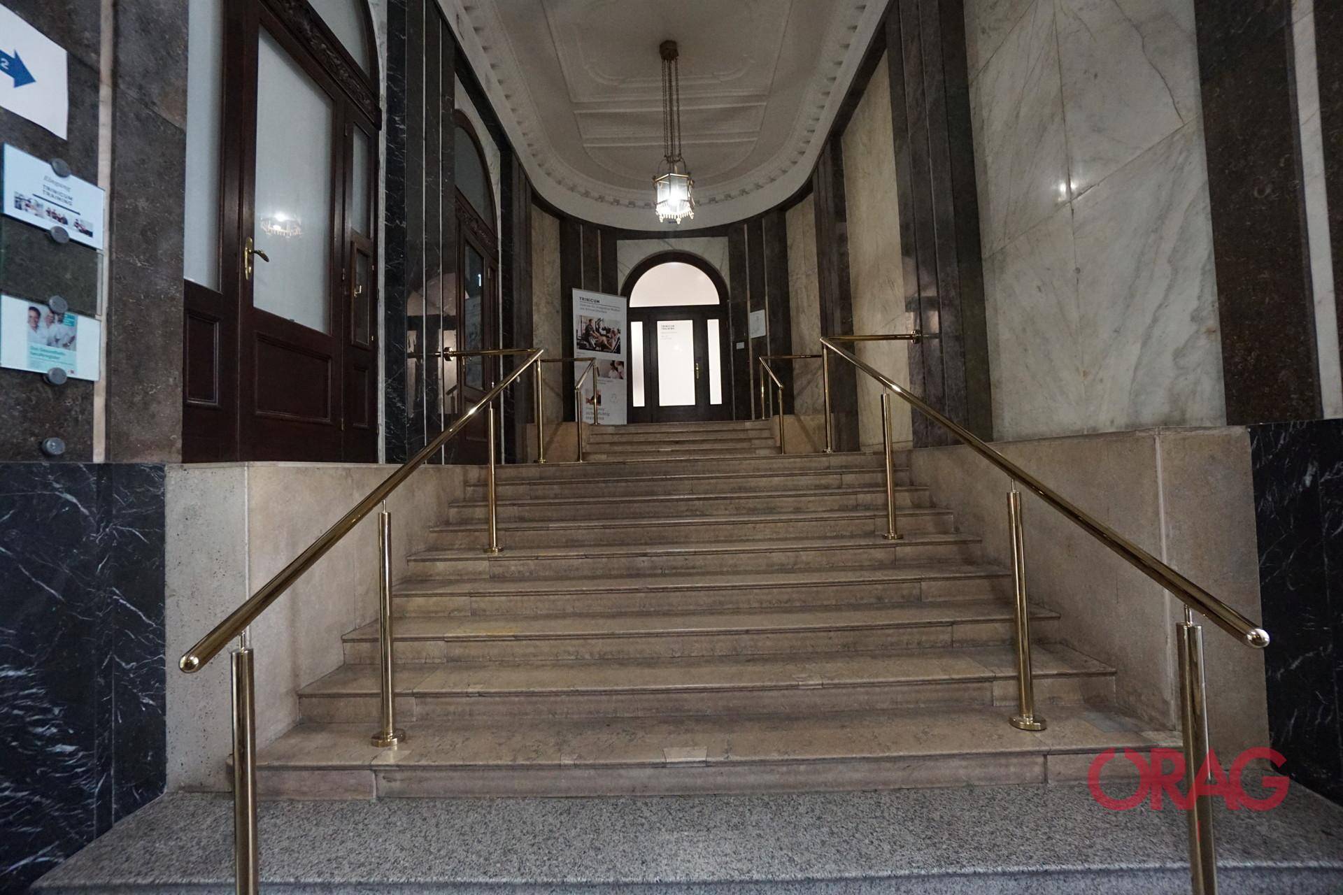 Repräsentativer Eingangsbereich mit breiter Steintreppe, Marmorwänden und eleganten Messinggeländern.