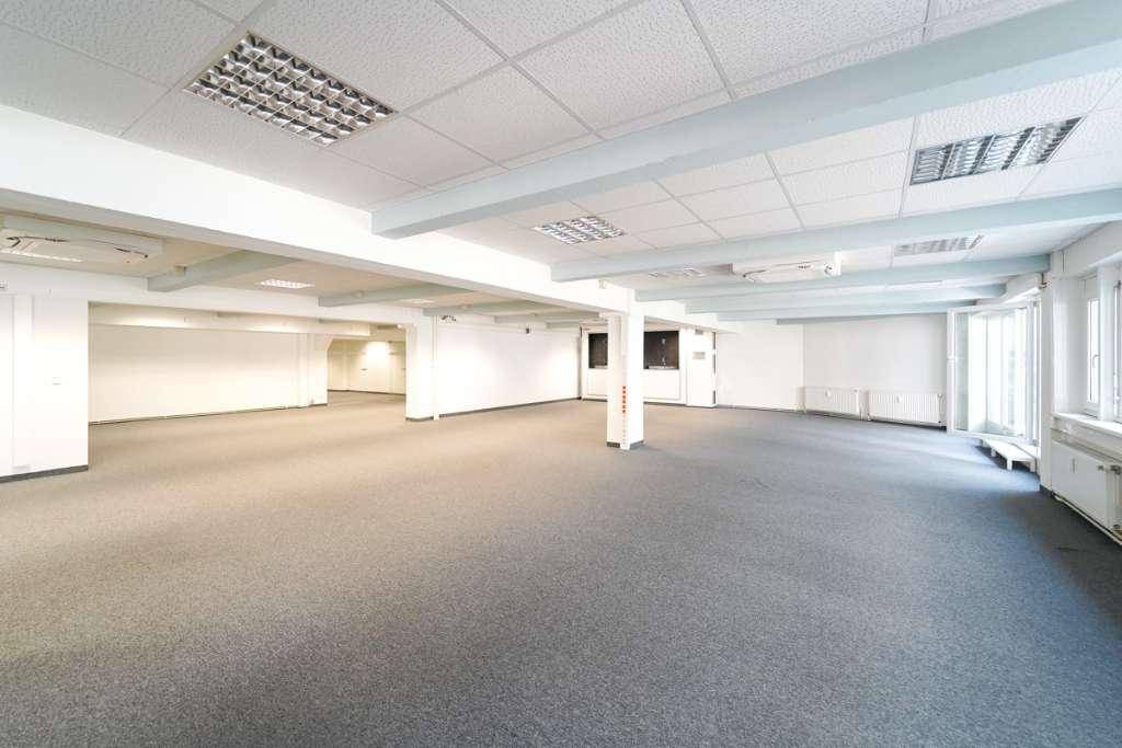Geräumiges, offenes Büro mit grauem Teppichboden, weißen Wänden und Deckenbeleuchtung.