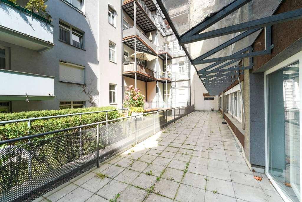 Lange, gepflasterte Terrasse mit Metallgeländer und Blick auf angrenzende Balkone.