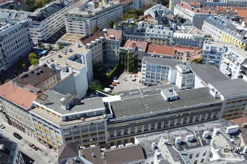Luftaufnahme eines großen Gebäudekomplexes mit Innenhof und umliegender Stadtbebauung.