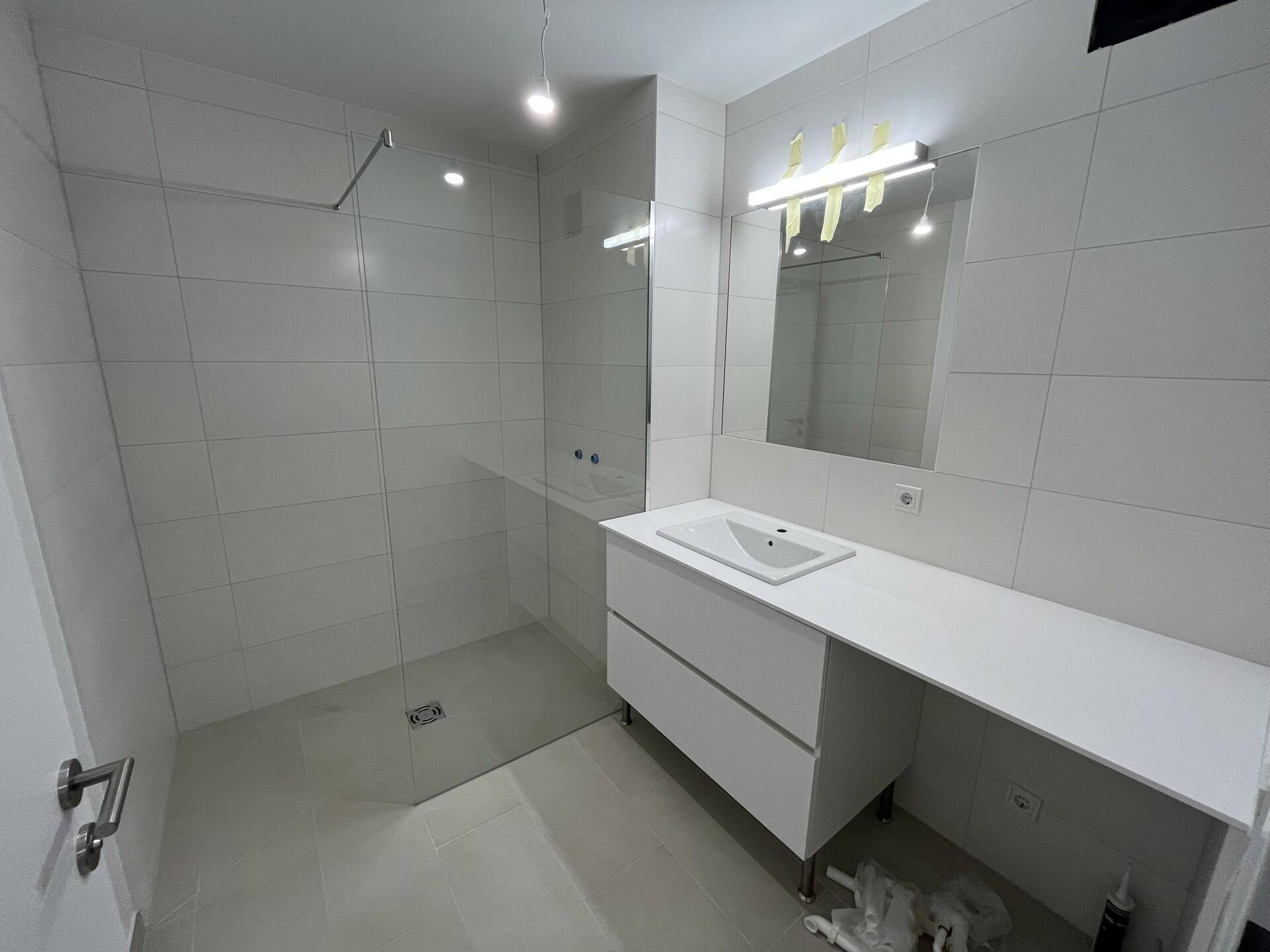 Modernes Badezimmer mit großer begehbarer Dusche, weißen Fliesen und Einzelwaschbecken.