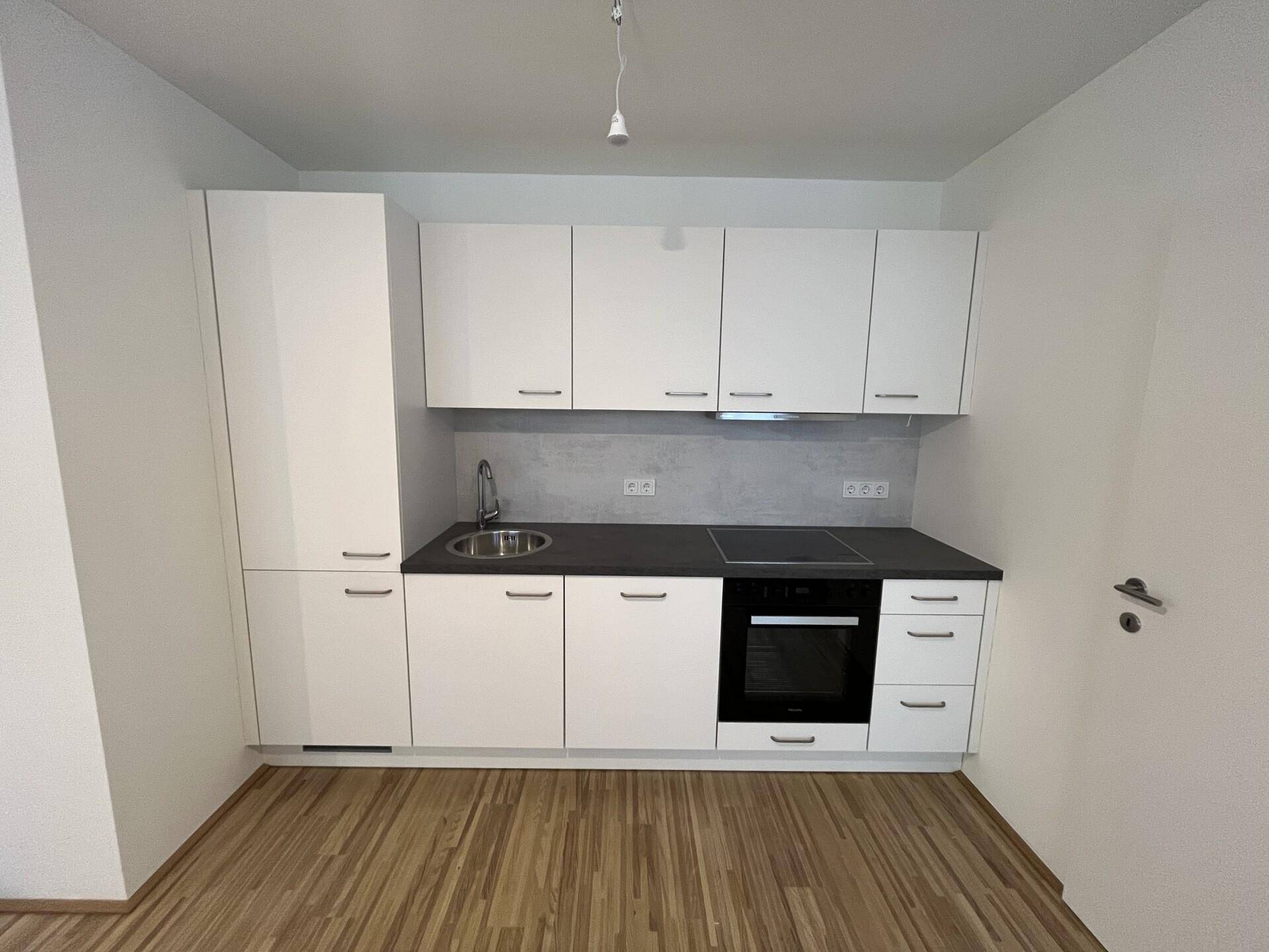 Kompakte moderne Küche mit weißen Schränken, Induktionskochfeld und integriertem Backofen.